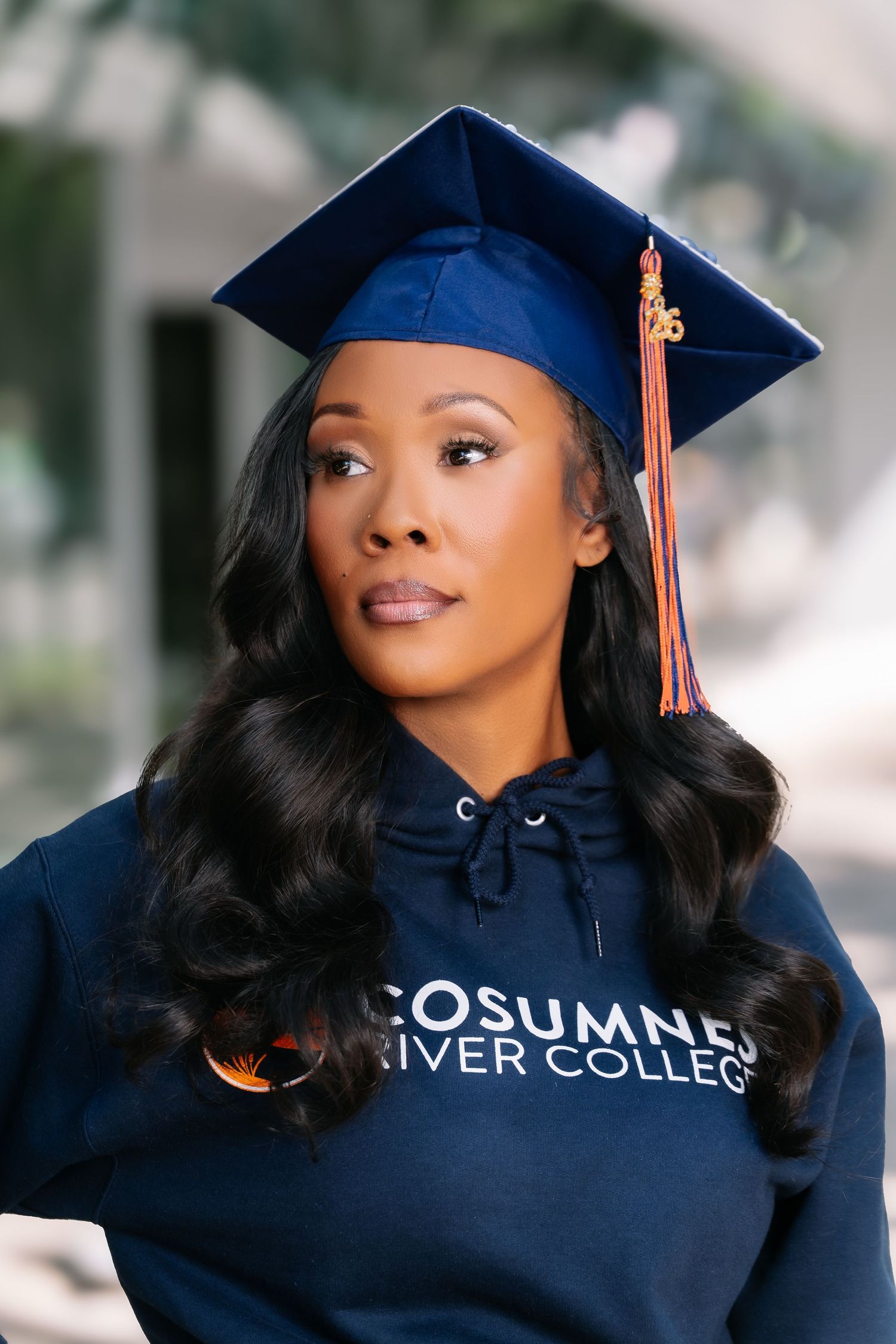 Close-up portrait of a Black woman in navy graduation cap and Cosumnes River College hoodie outdoors.