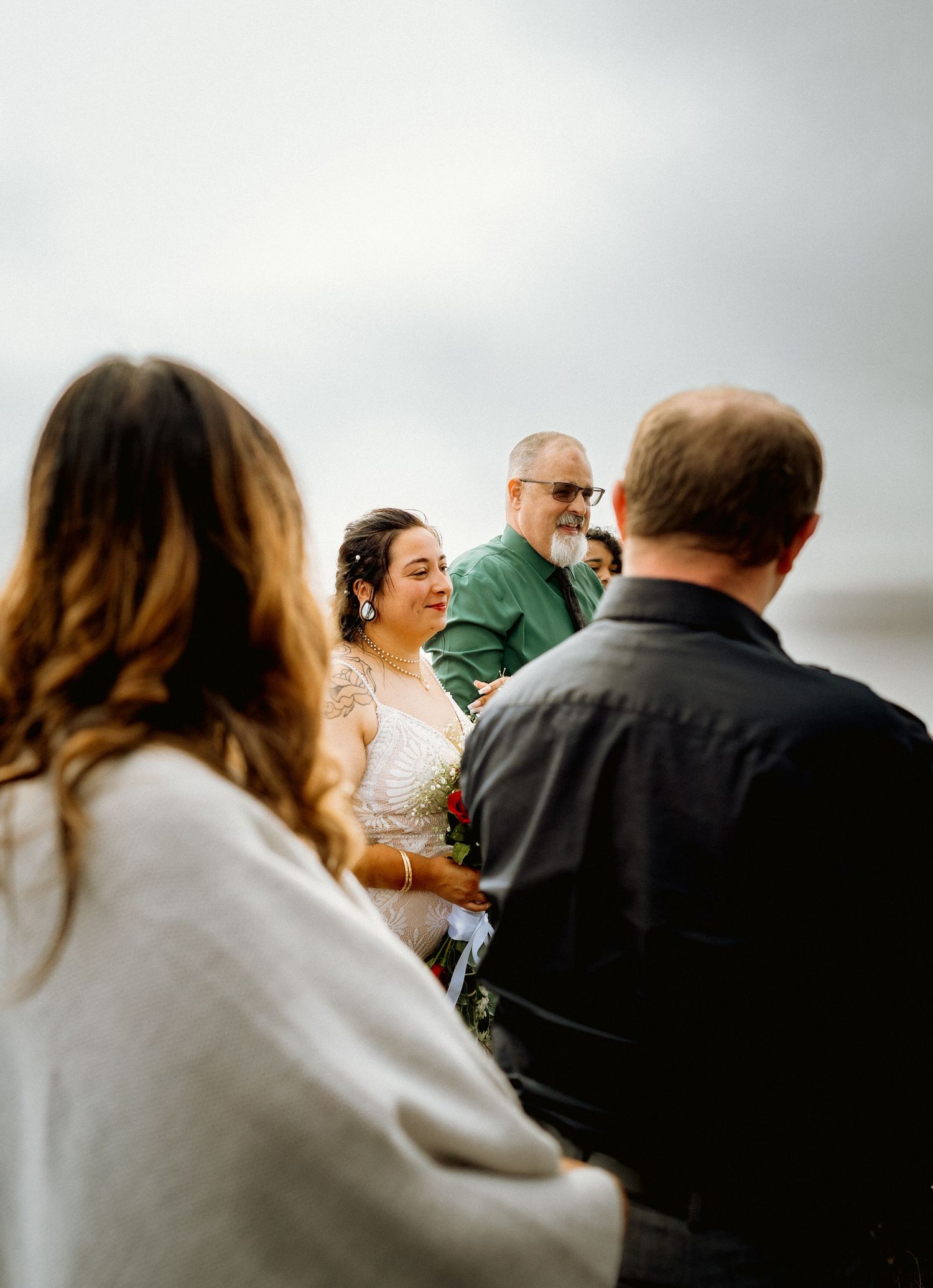 Smiling bride in lace gown exchanges vows with groom at outdoor beach wedding ceremony.