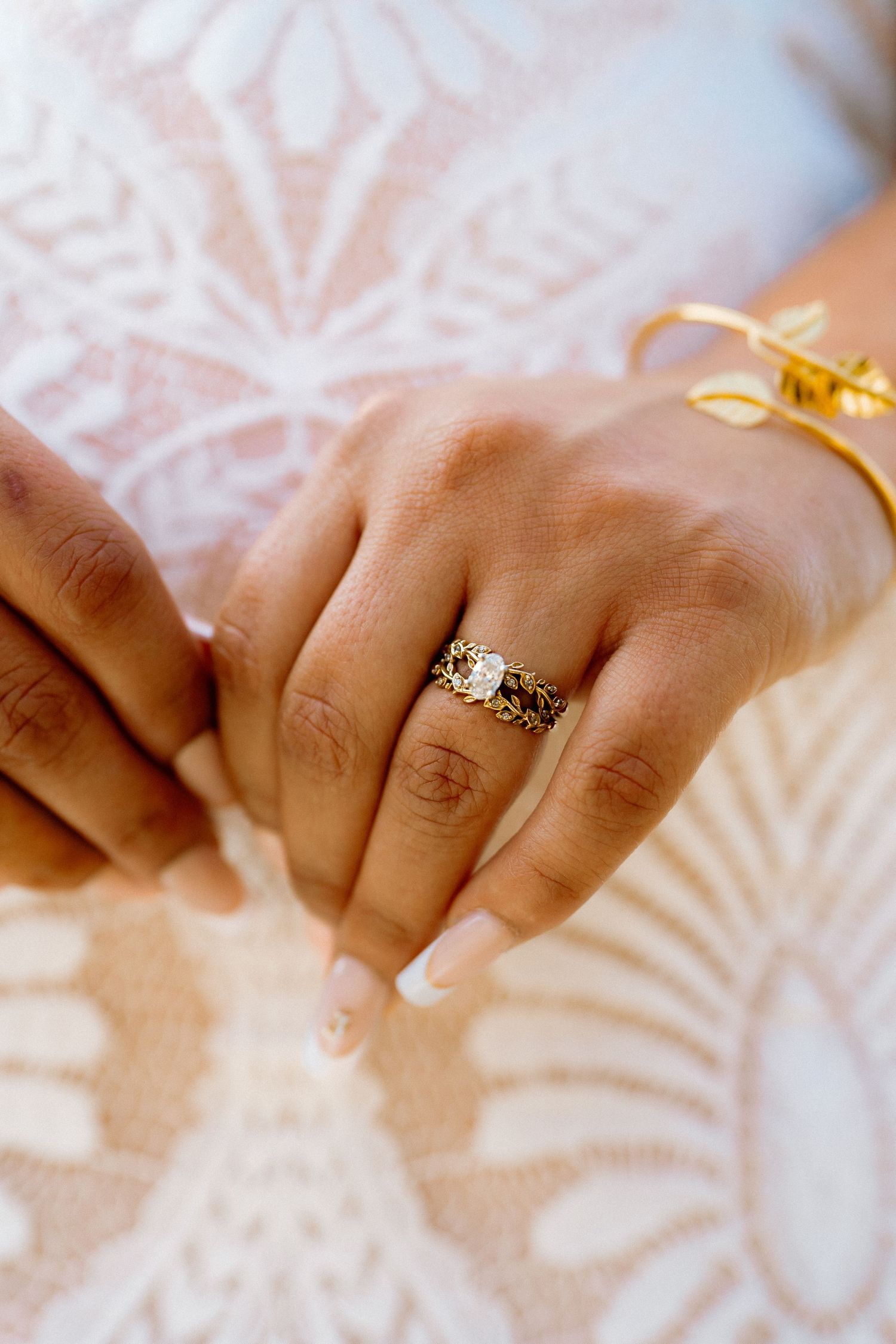 Close-up of a bride's hands displaying a gold diamond engagement ring and gold bangle bracelet.