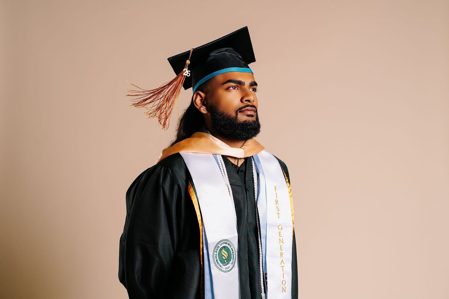 Young Black man in black graduation cap and gown with gold honor stole poses proudly.