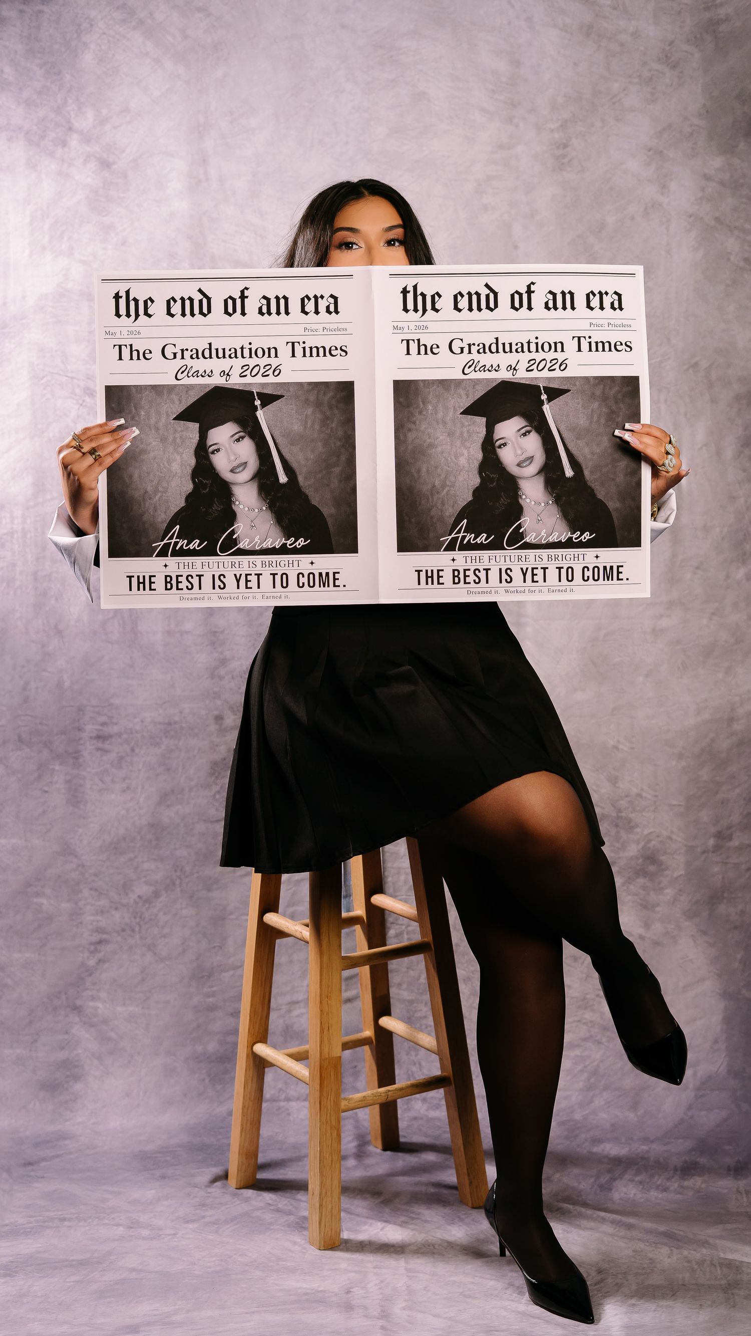 Woman holding graduation newspaper prop reading The End of an Era Class of 2026.