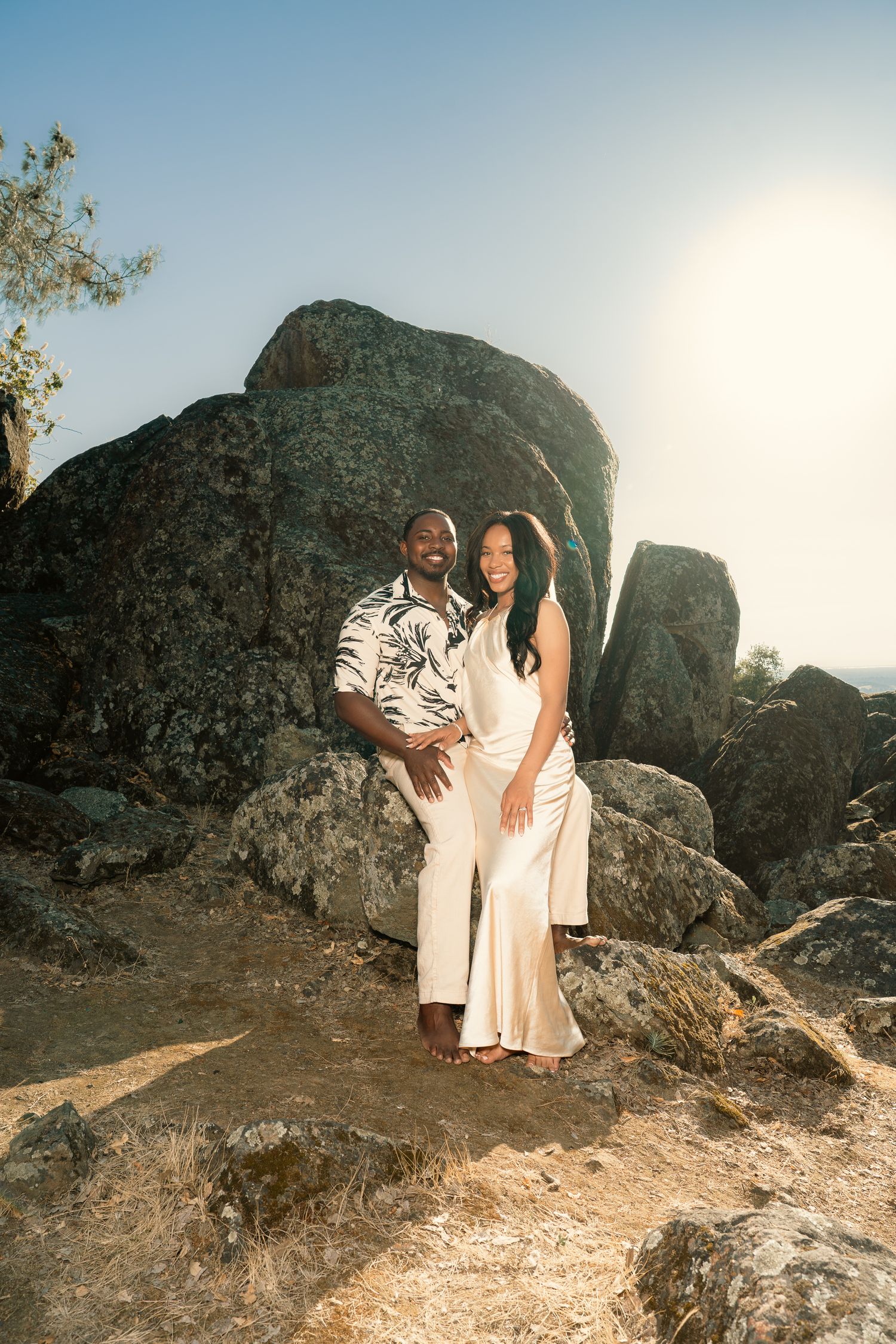 Wedding couple posing together among large rocks in a sun-drenched outdoor landscape.