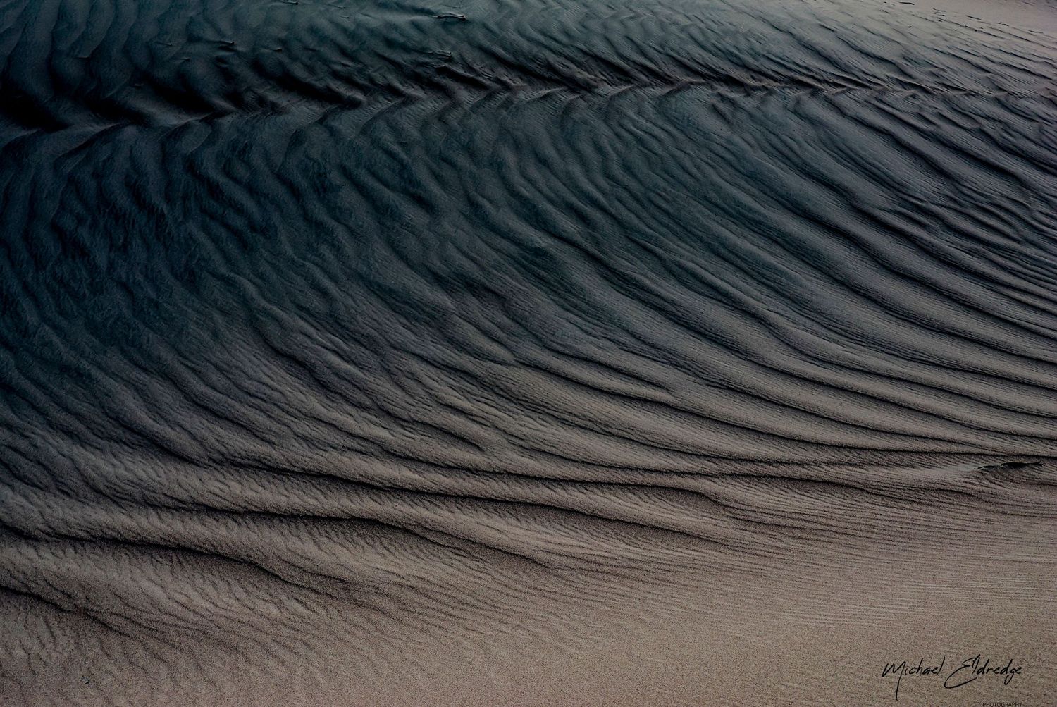 Abstract pattern of rippling sand dunes in dramatic light and shadow.