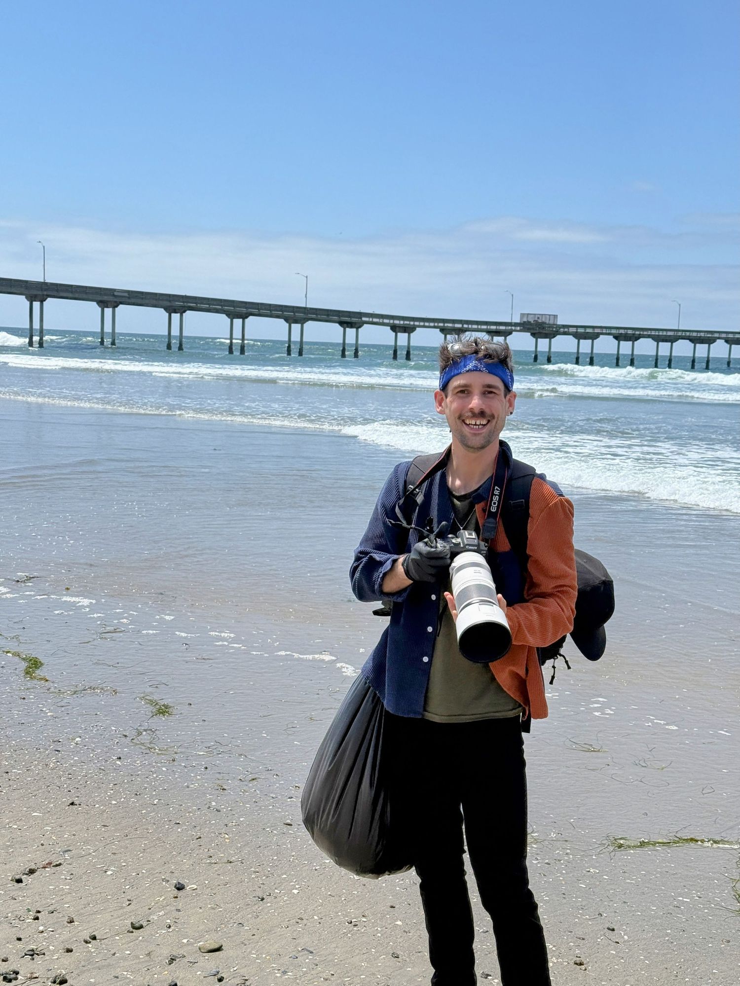 People enjoying a beach day with photography equipment near an ocean pier.