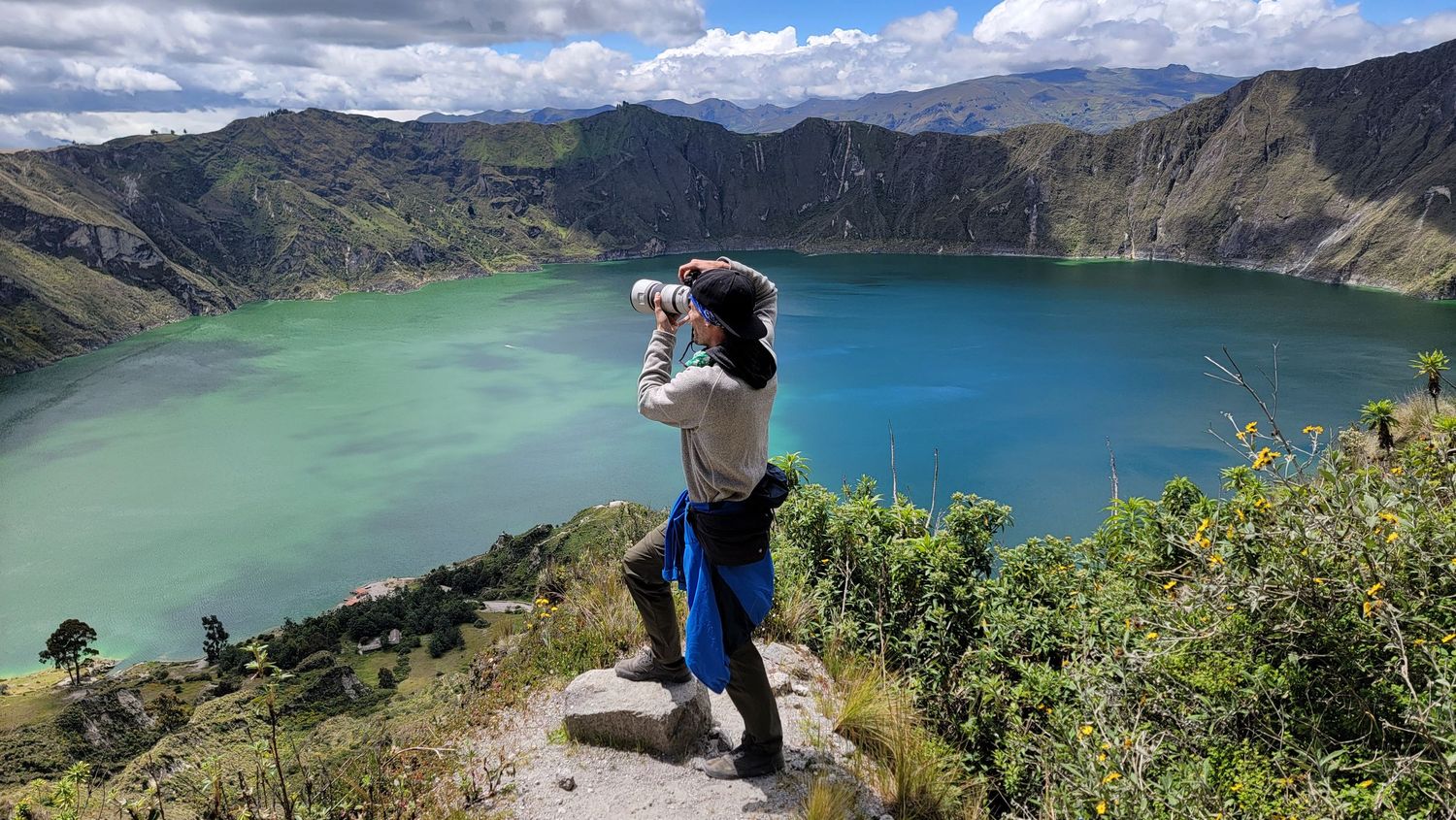 Panoramic mountain landscape with turquoise lake surrounded by steep cliffs and cloudy skies.