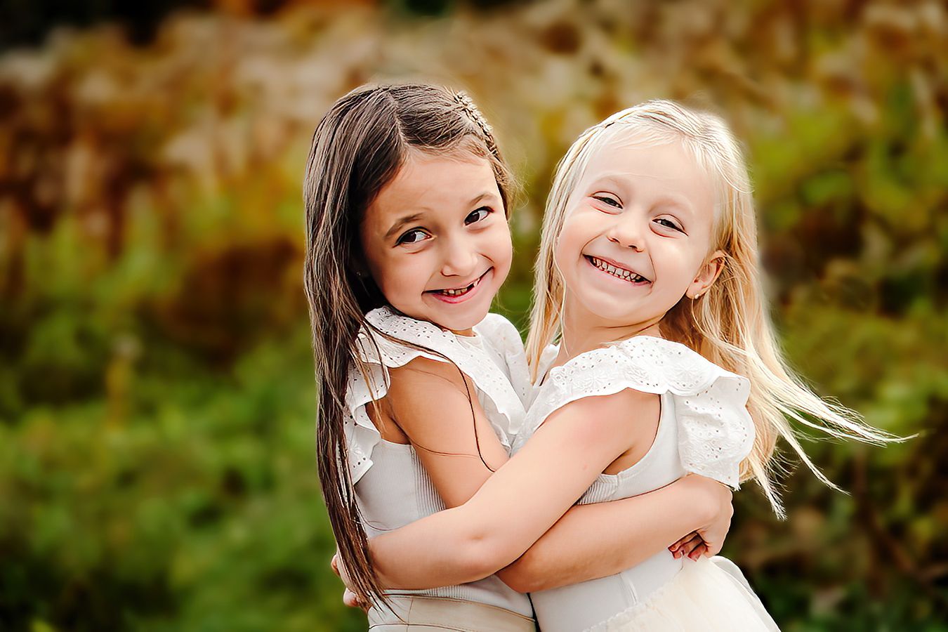 Two young girls in coordinating outfits embracing and laughing outdoors in fall