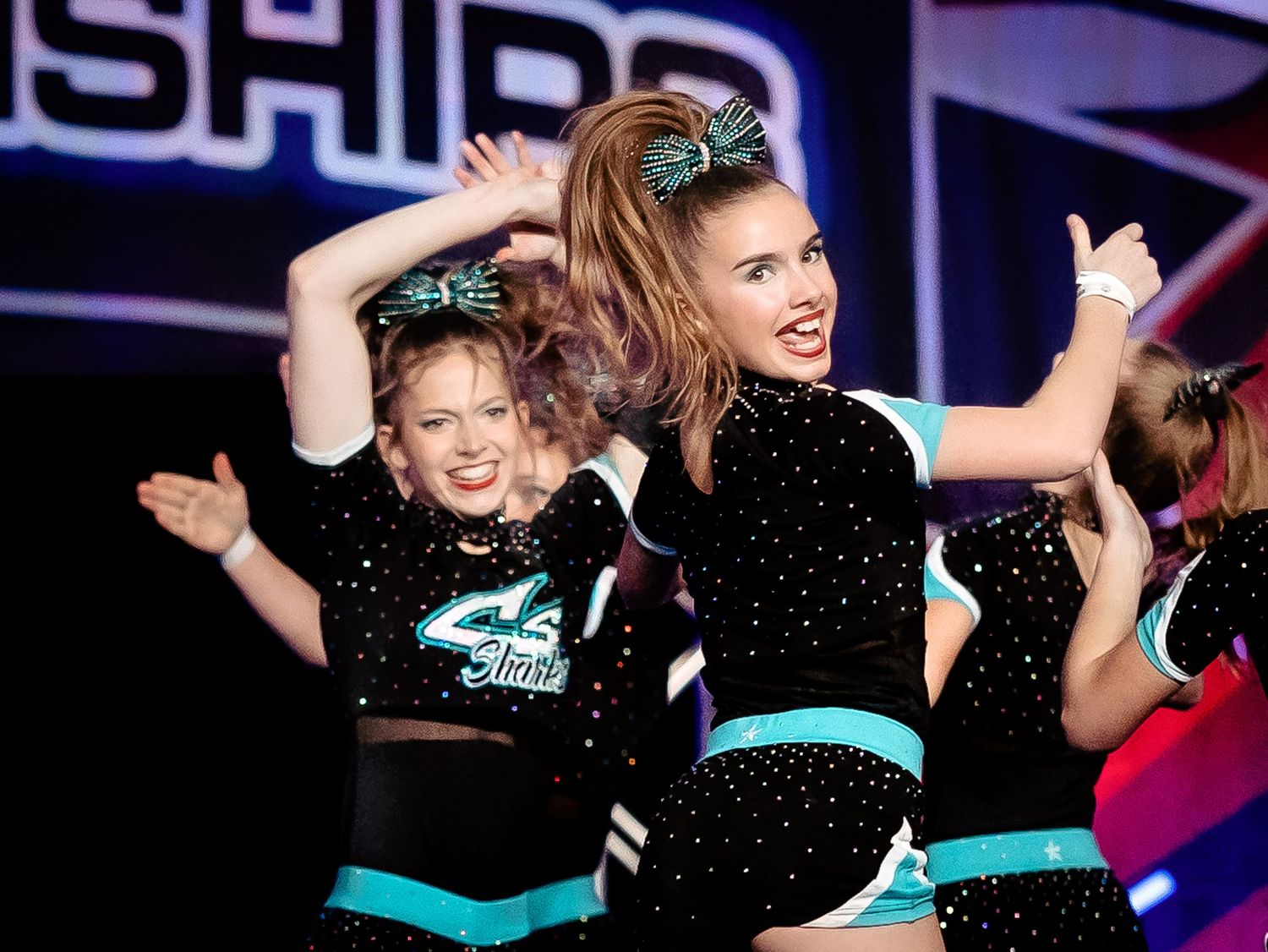 Two young cheerleaders celebrating with arms raised on a championship stage
