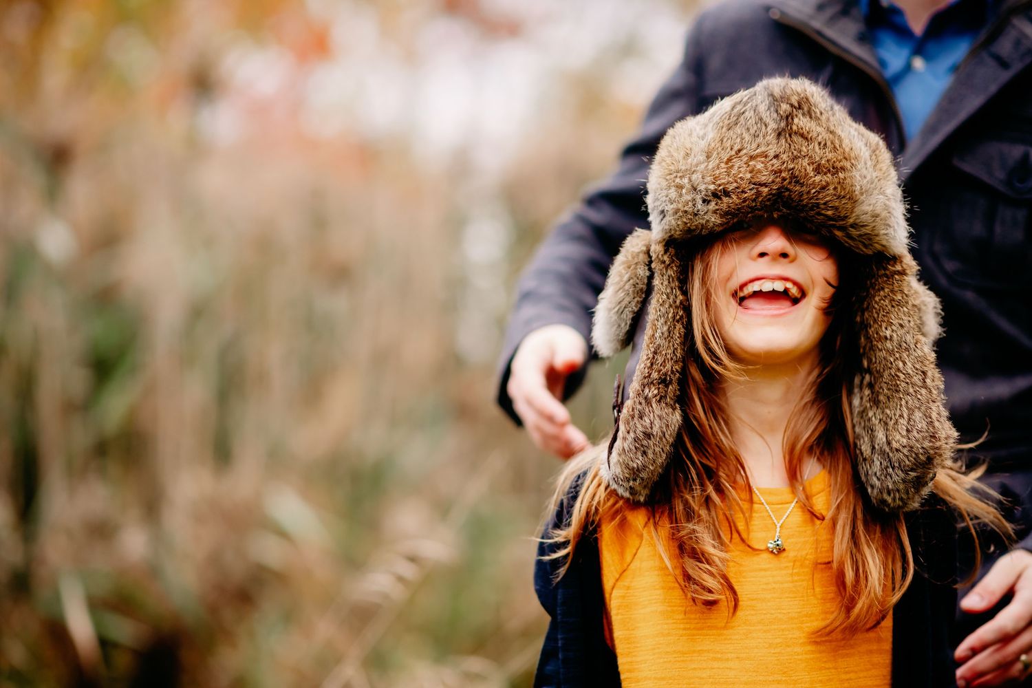 CHILD laughing joyfully wearing a fur trapper hat in a golden autumn outdoor setting