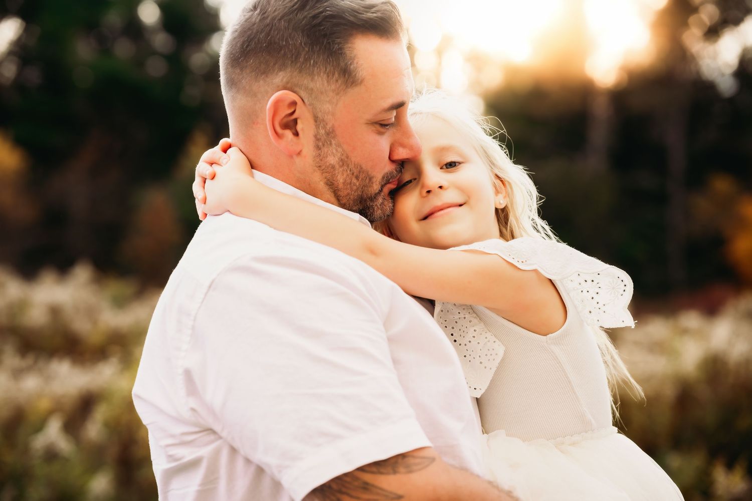 Father holding a young daughter close outdoors, sharing a sweet golden-hour embrace in fall