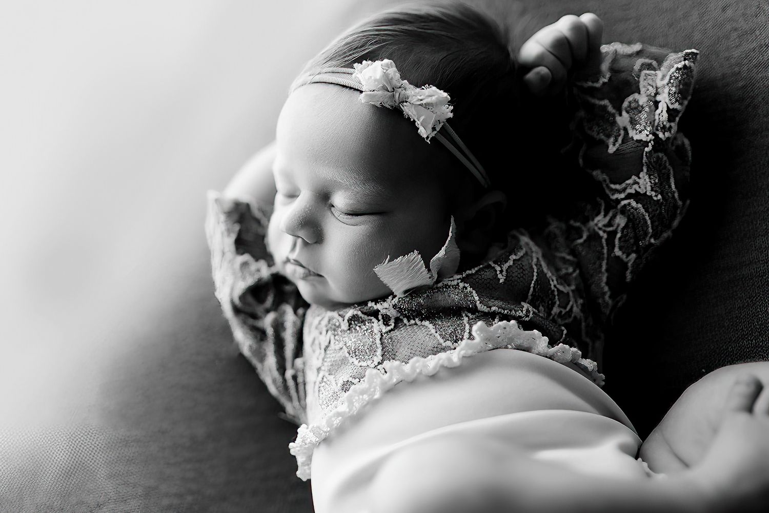 Black and white close-up of a sleeping newborn baby wrapped in lace fabric, peaceful portrait