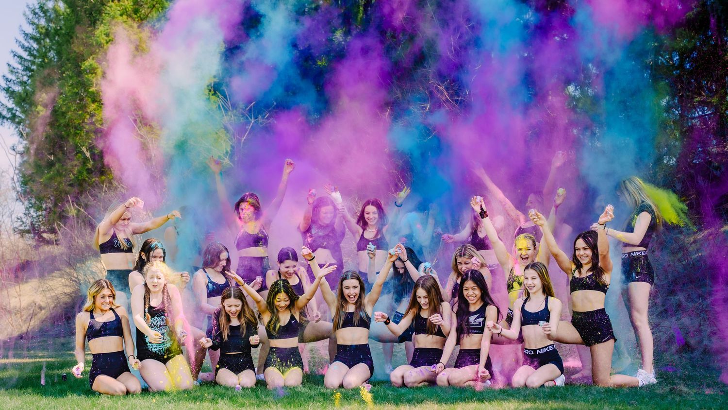 Cheerleading team celebrating with colorful powder explosions in an outdoor field, vibrant action shot