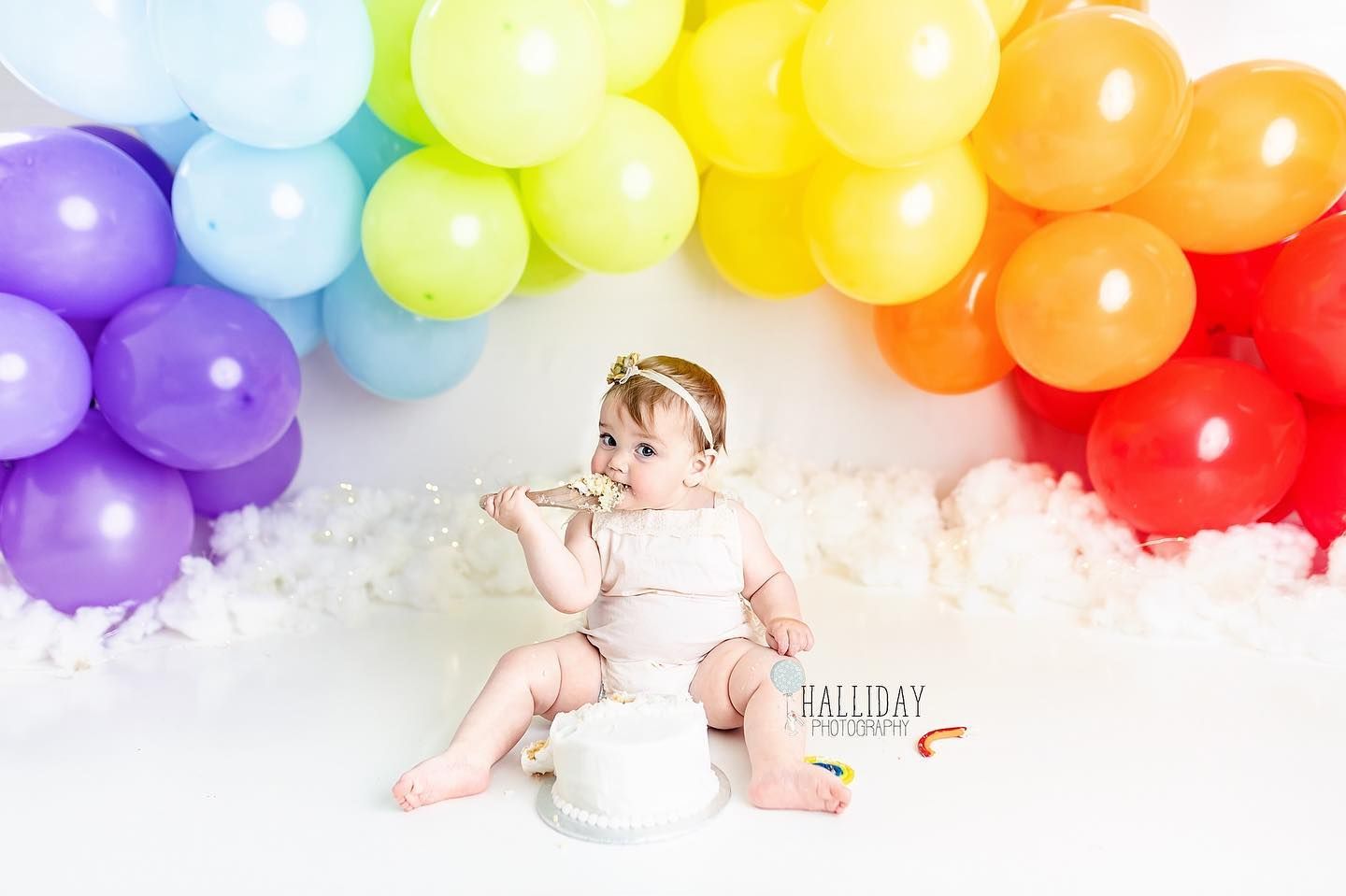 First birthday milestone portrait with rainbow balloon backdrop photographed in studio