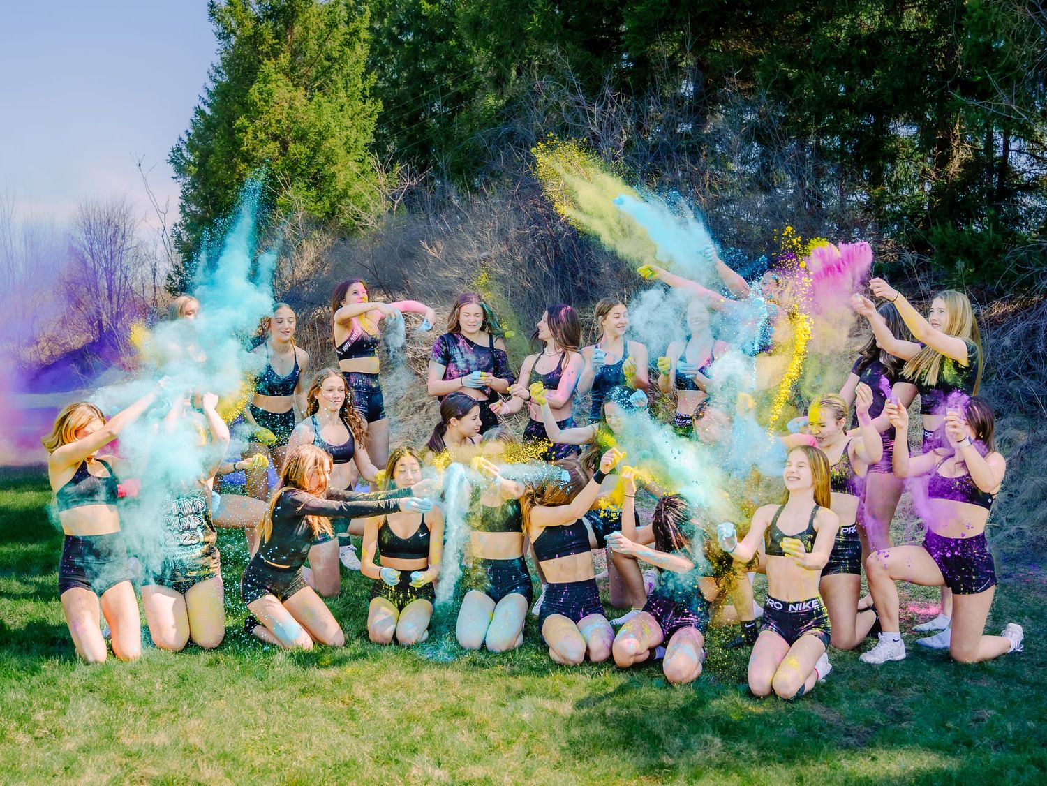 Cheerleading team celebrating with colorful powder explosions in an outdoor field, vibrant action shot
