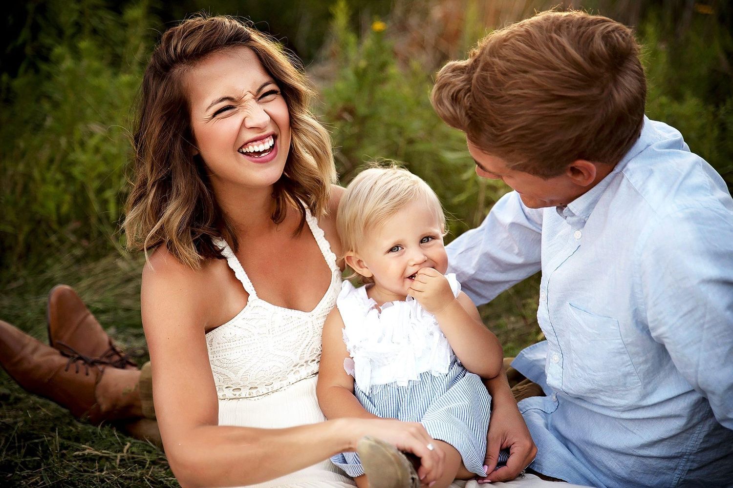Mother smiling at a toddler while a partner looks on lovingly, outdoor family portrait
