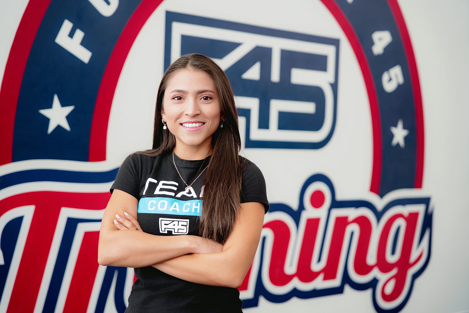 Woman smiling with arms crossed in front of a F45 Team Training branded gym logo, commercial branding portrait