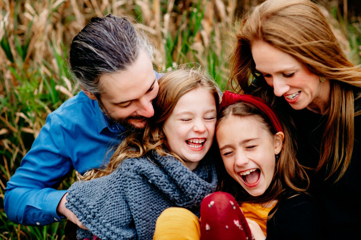 Joyful family of three laughing together outdoors, mother and father embracing a young child