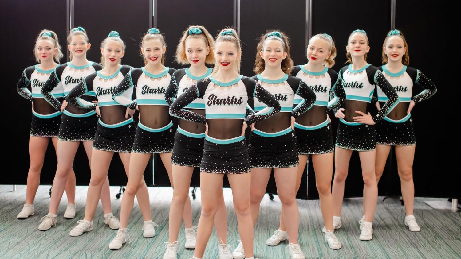 Large cheerleading team in matching uniforms lined up on a competition floor