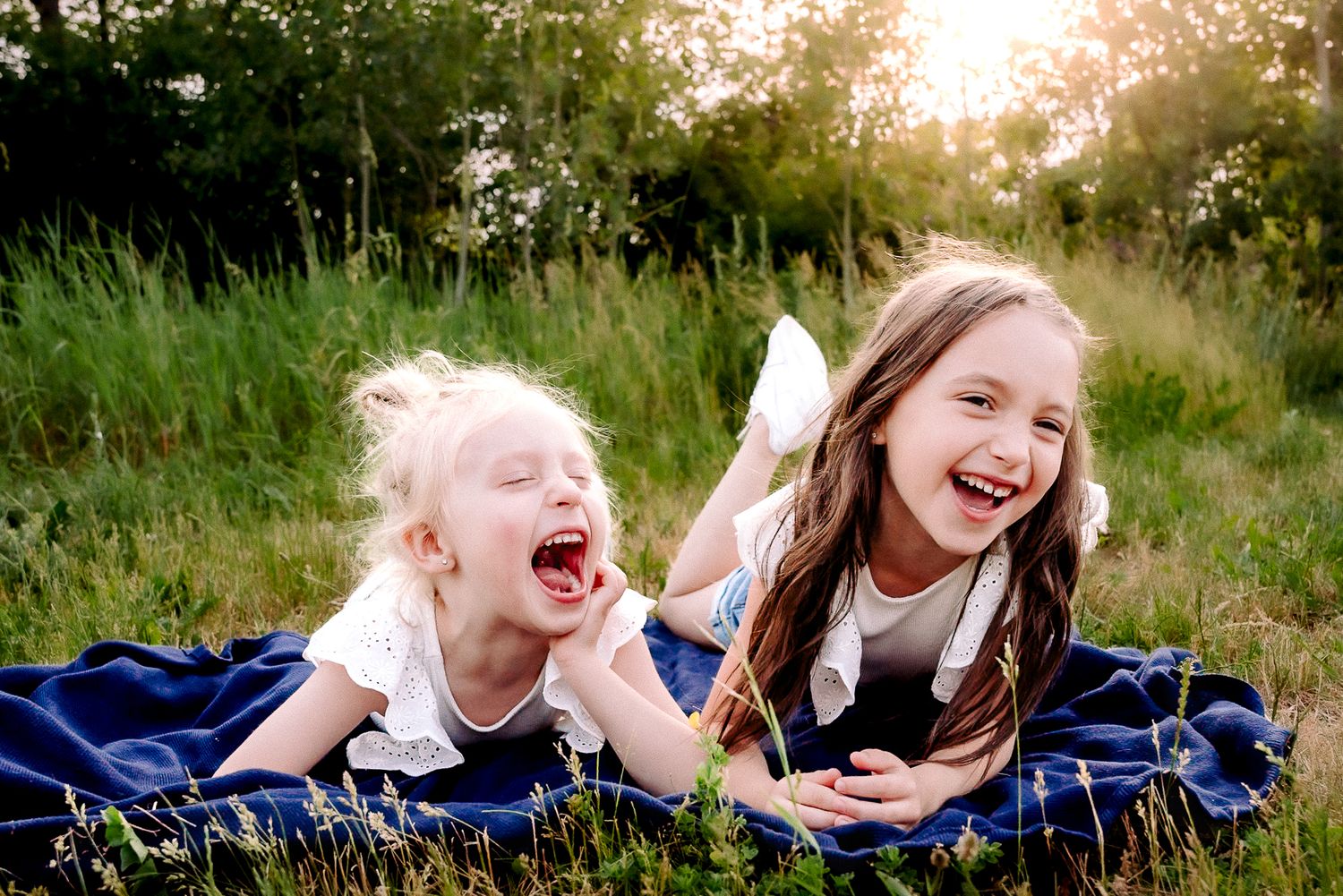 Two young sisters lying in a field laughing together during an outdoor lifestyle family photo session