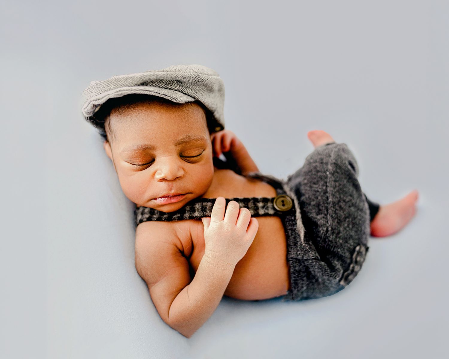 Newborn baby in a newsboy cap and suspenders posed in a studio newborn portrait