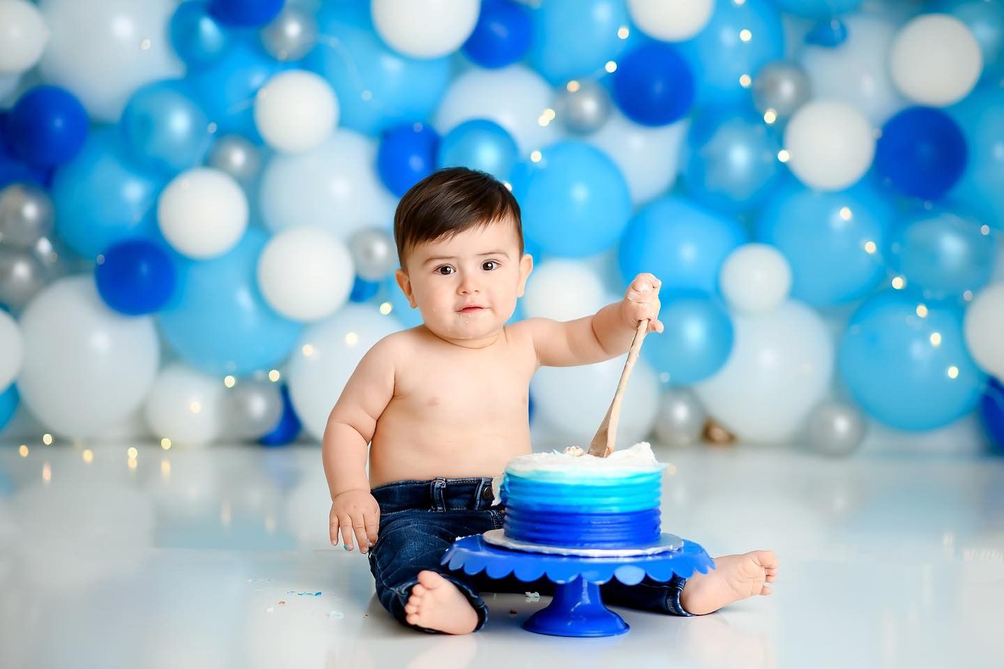 Baby celebrating a cake smash session with blue balloon backdrop in studio