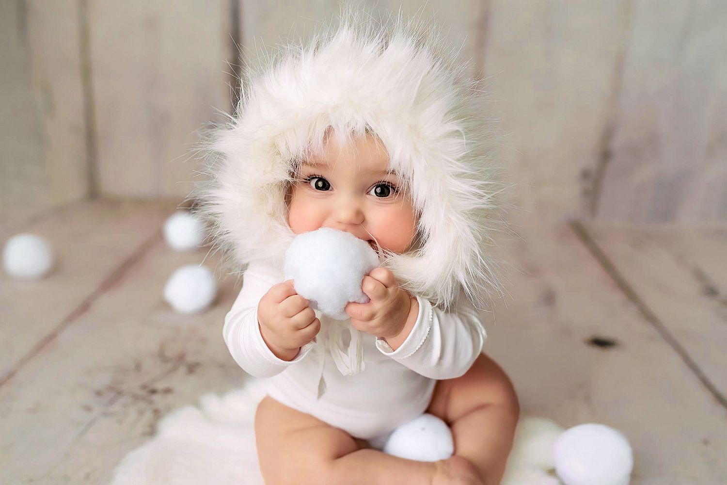 Baby milestone portrait wearing a soft bonnet and holding props in a neutral studio setting