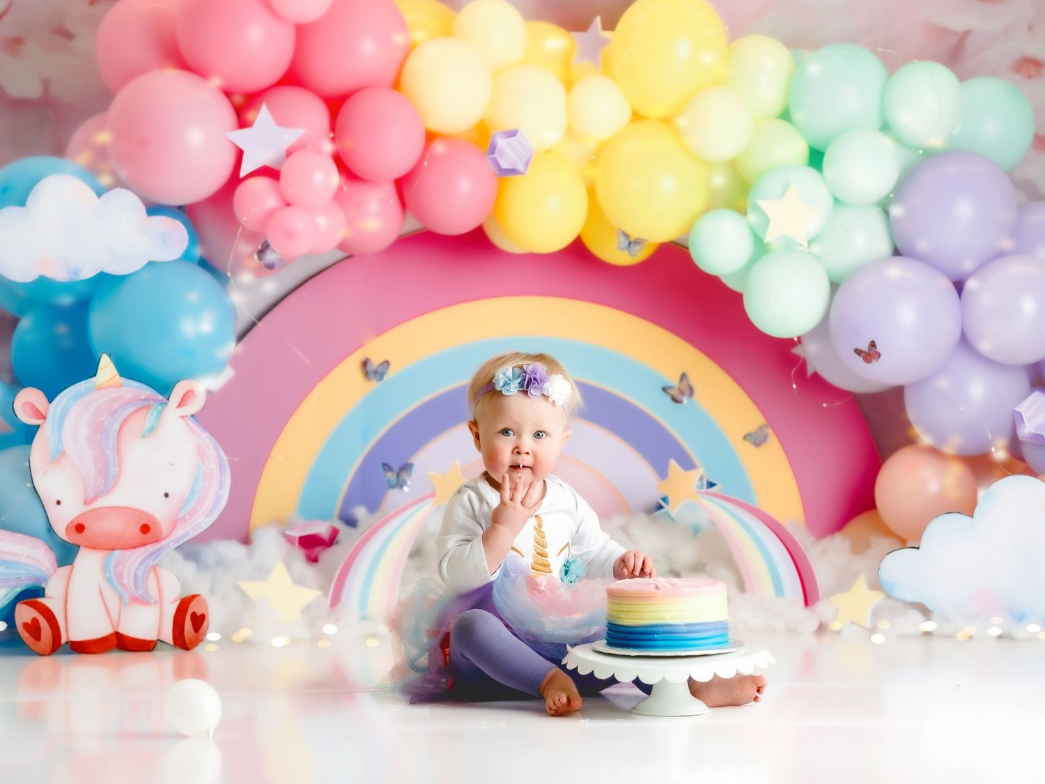 First birthday cake smash portrait with rainbow backdrop and pastel balloon decor