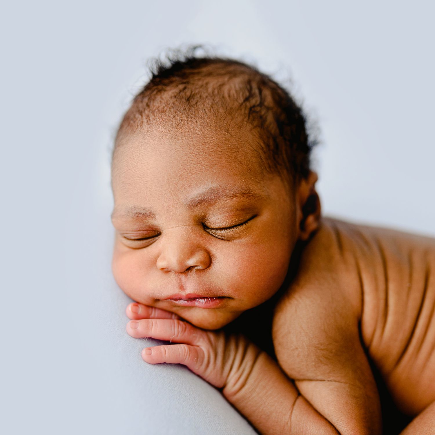 Close-up portrait of a sleeping newborn baby with delicate features on a light blue background