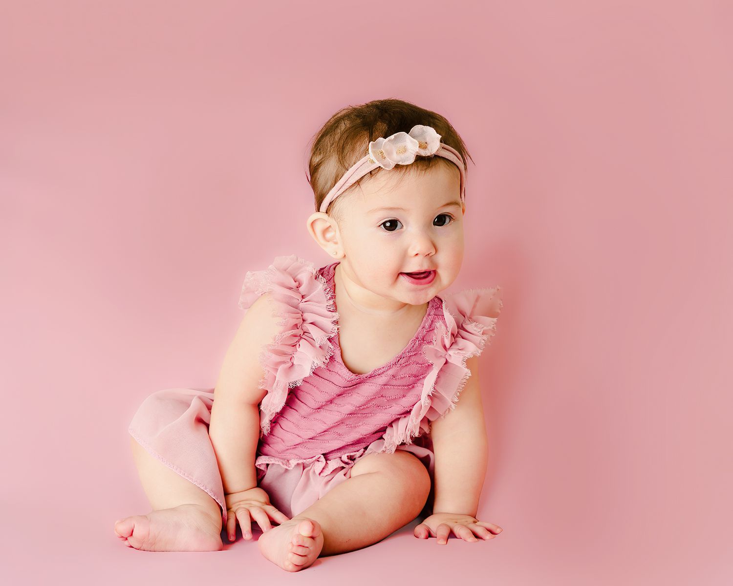 Baby in a pink outfit sitting on a pink background in a bright studio portrait