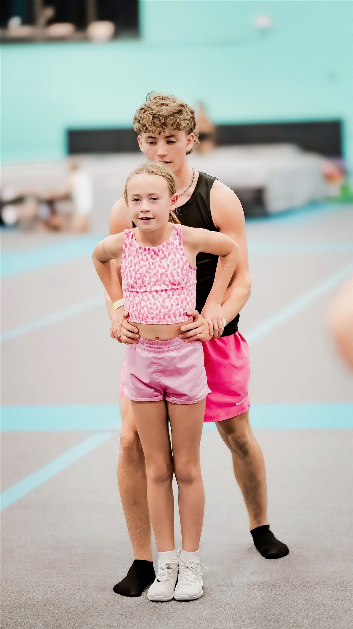 Two young cheerleaders in pink outfits performing together in a gym
