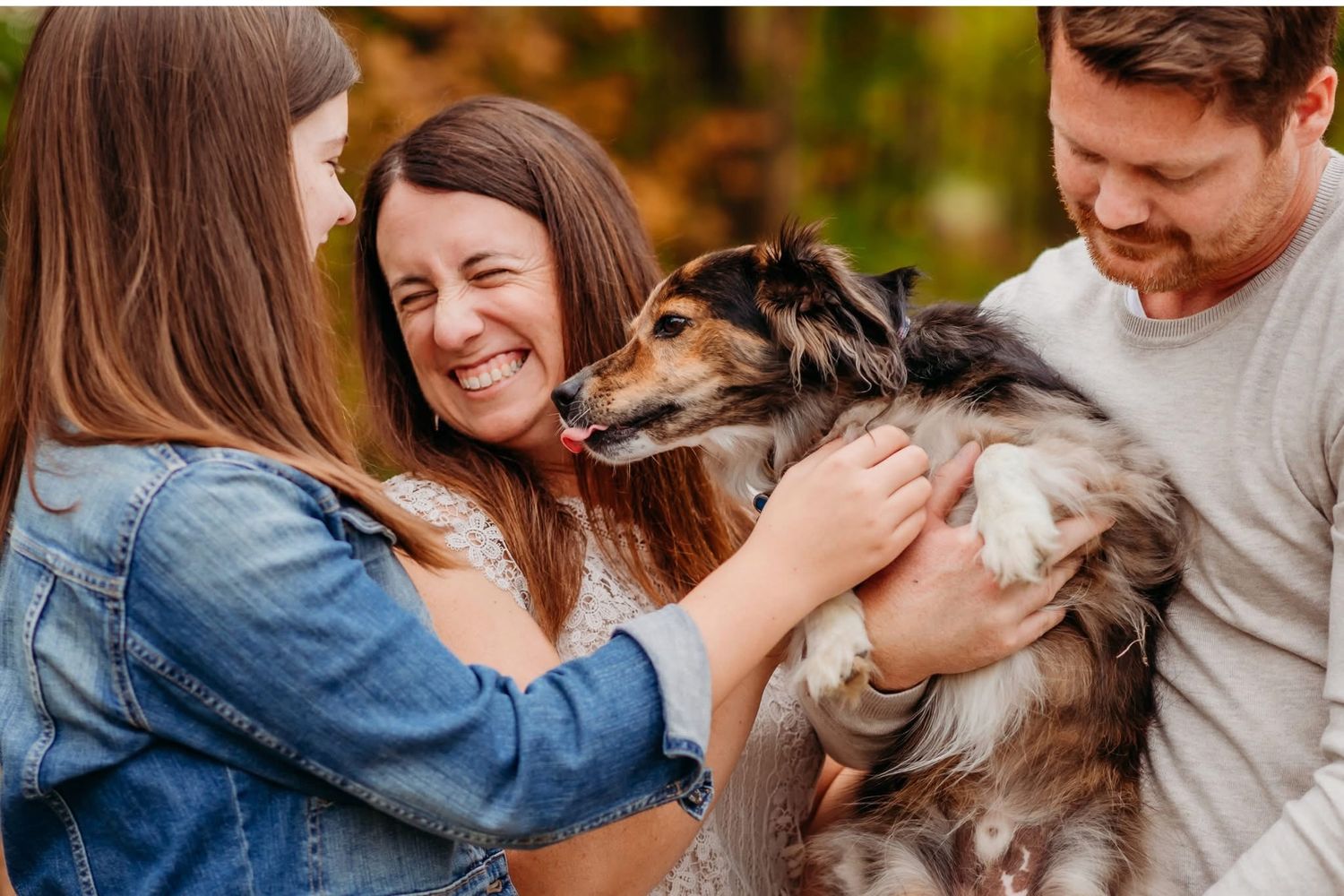 Couple laughing with a dog in autumn foliage, golden tones in the background