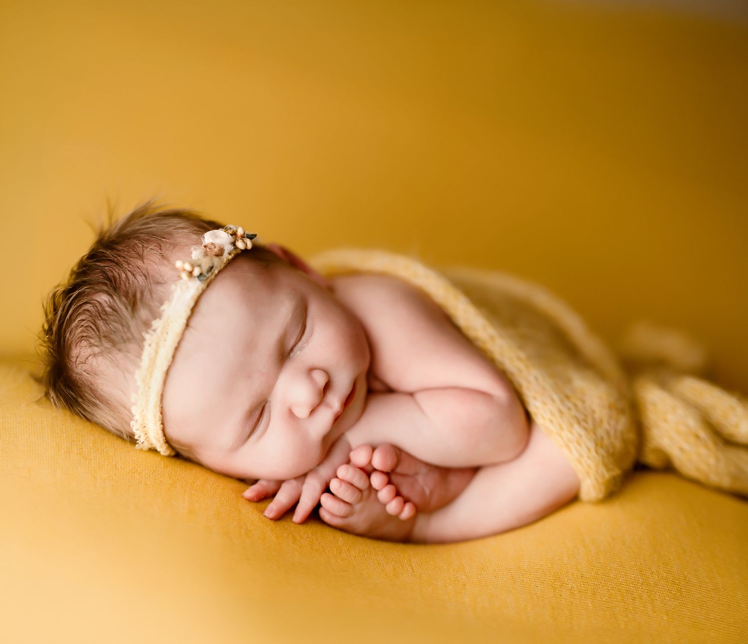 Sleeping newborn baby wrapped in a mustard yellow blanket with a delicate headband