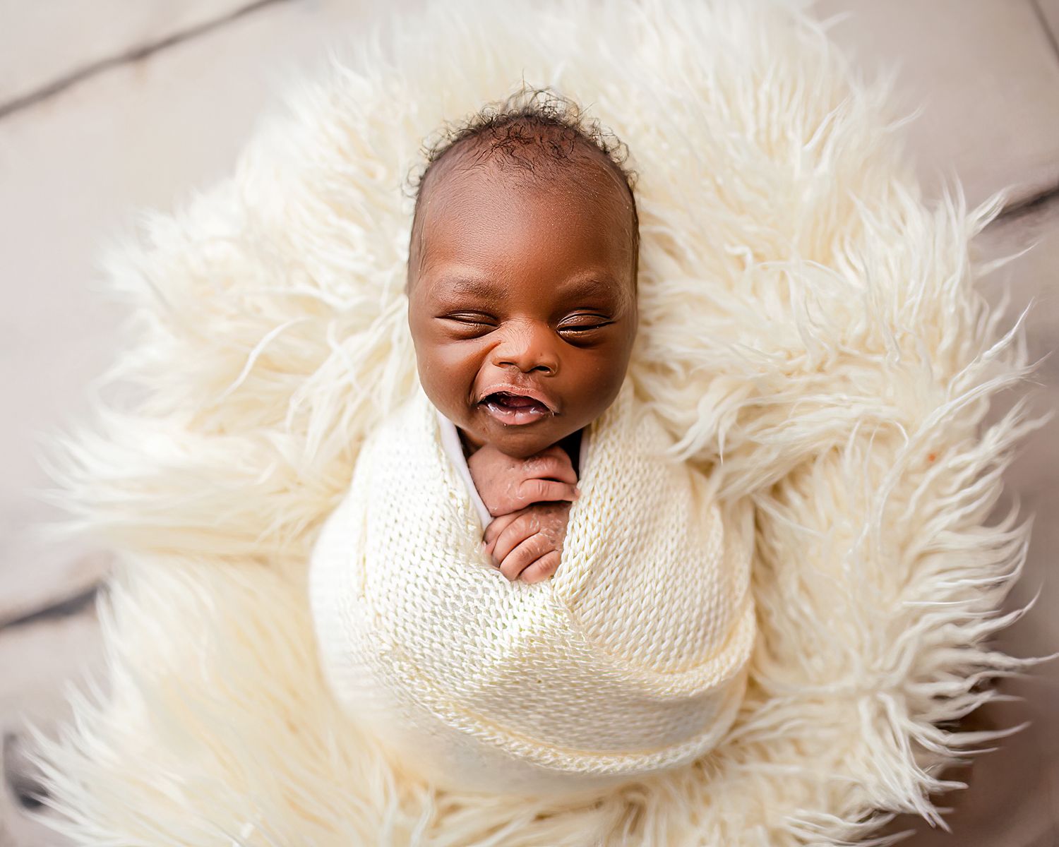 Smiling newborn baby swaddled in white wrap lying on a fluffy white surface