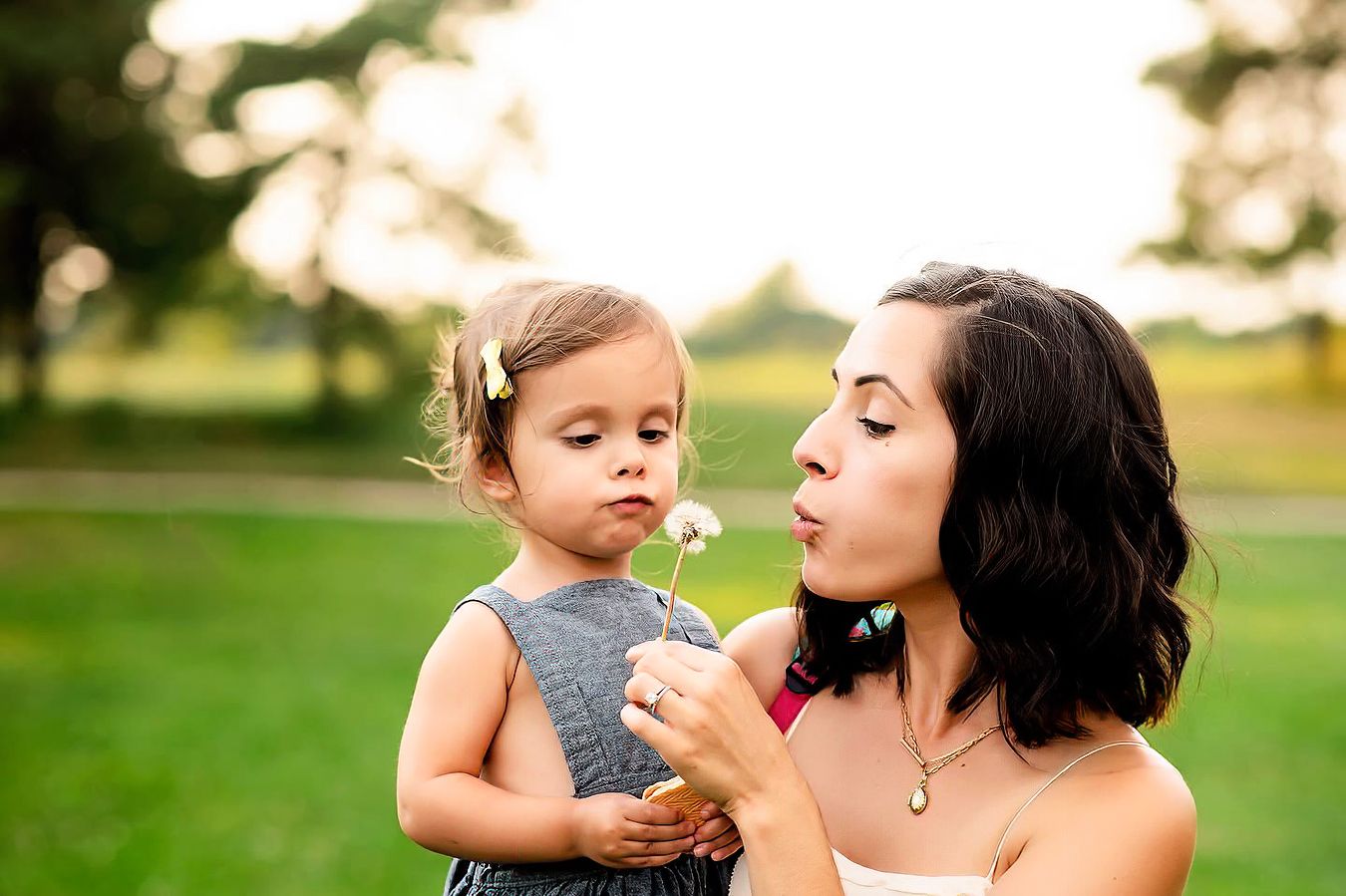 Mother bending down to a toddler outdoors in a golden-hour field, lifestyle family portrait