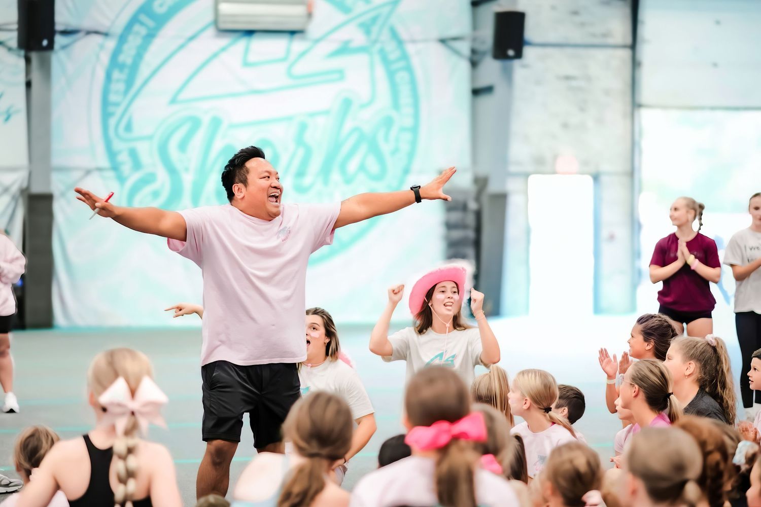 Cheerleading coach celebrating with arms wide open surrounded by enthusiastic young athletes in a gym