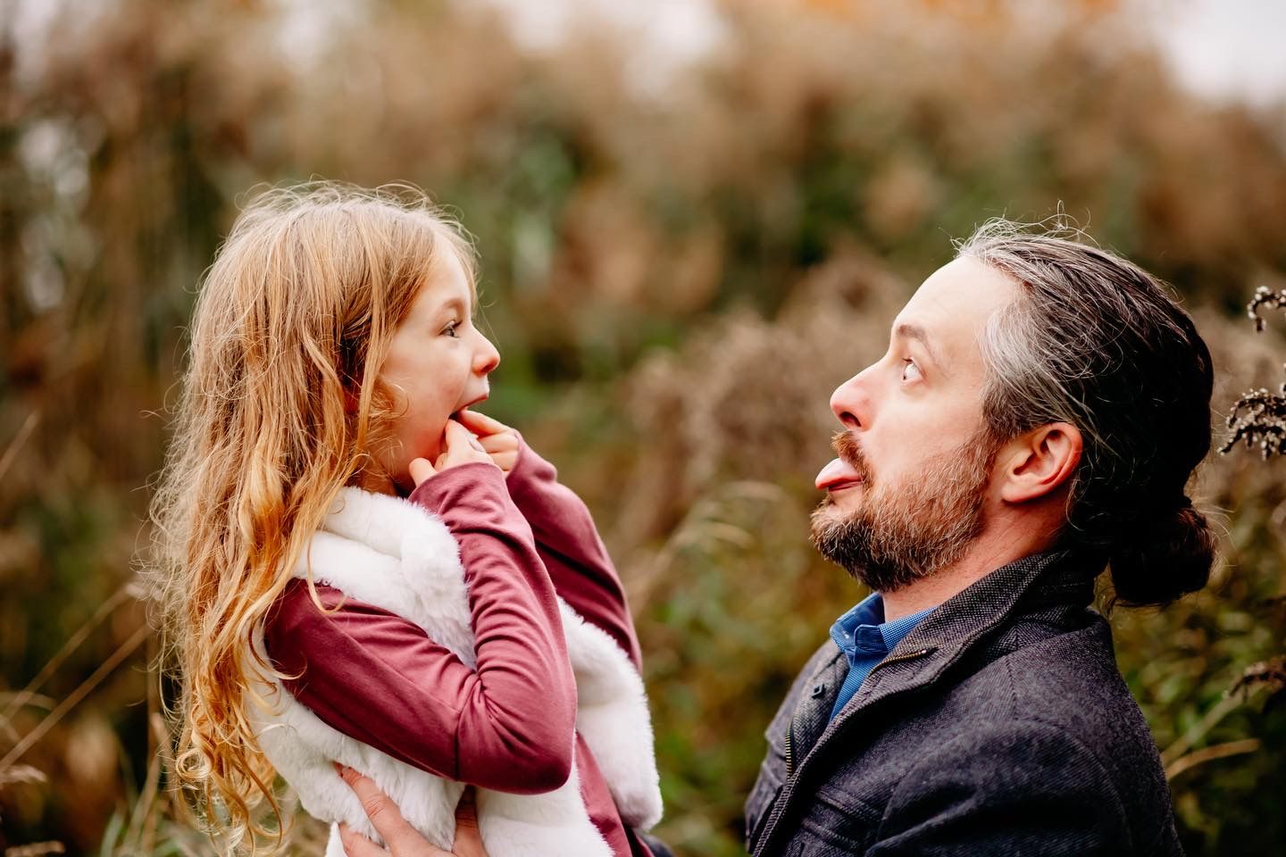 Father holding a young girl up close face to face, sharing a tender moment outdoors in autumn