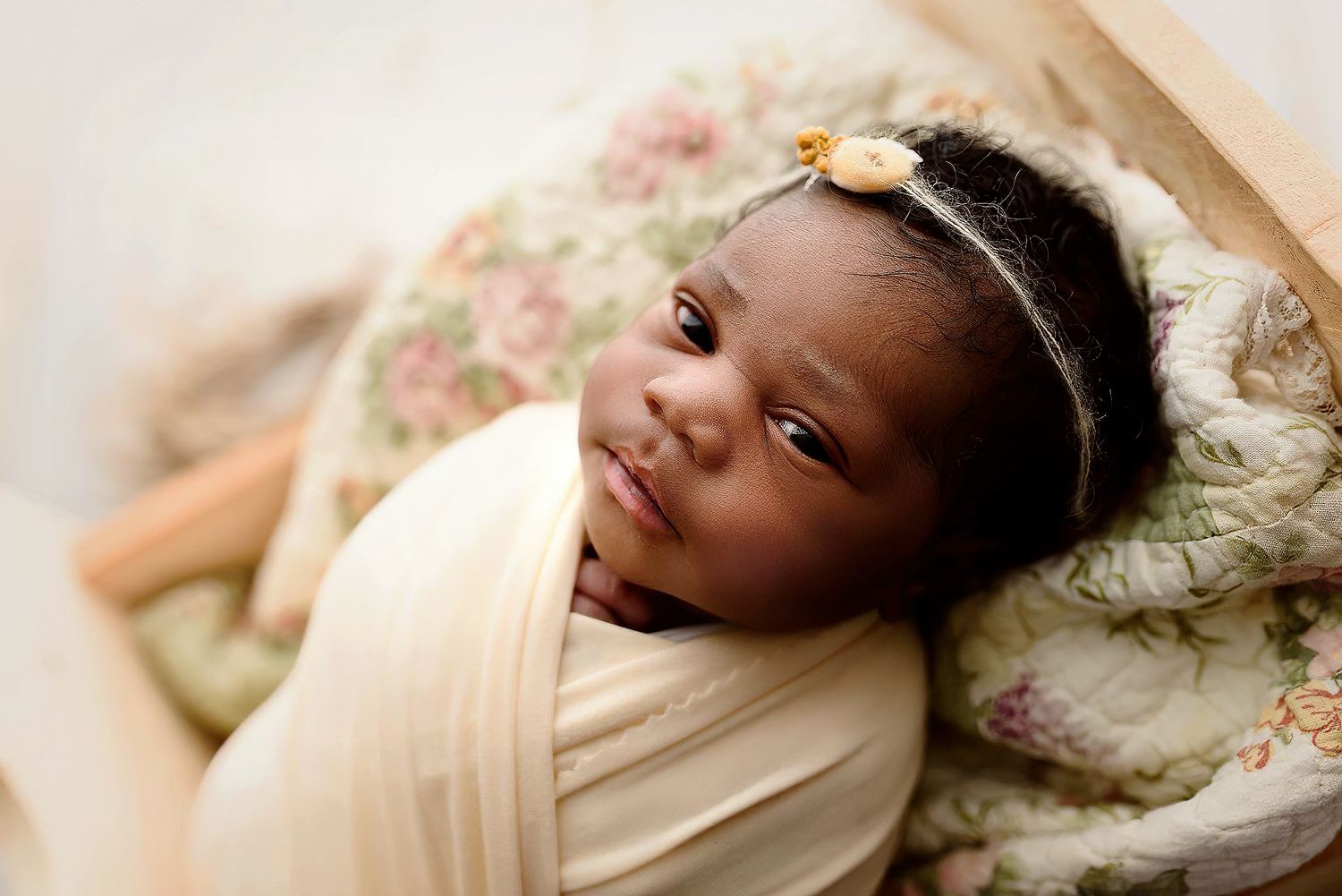 Sleeping newborn baby with a floral headband wrapped in cream fabric on a floral blanket