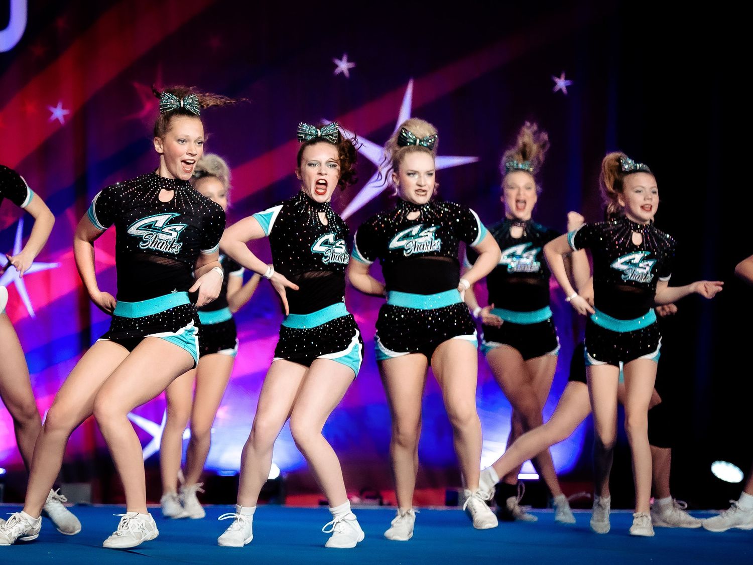 Youth cheerleading team posing in black and teal uniforms on a competition floor