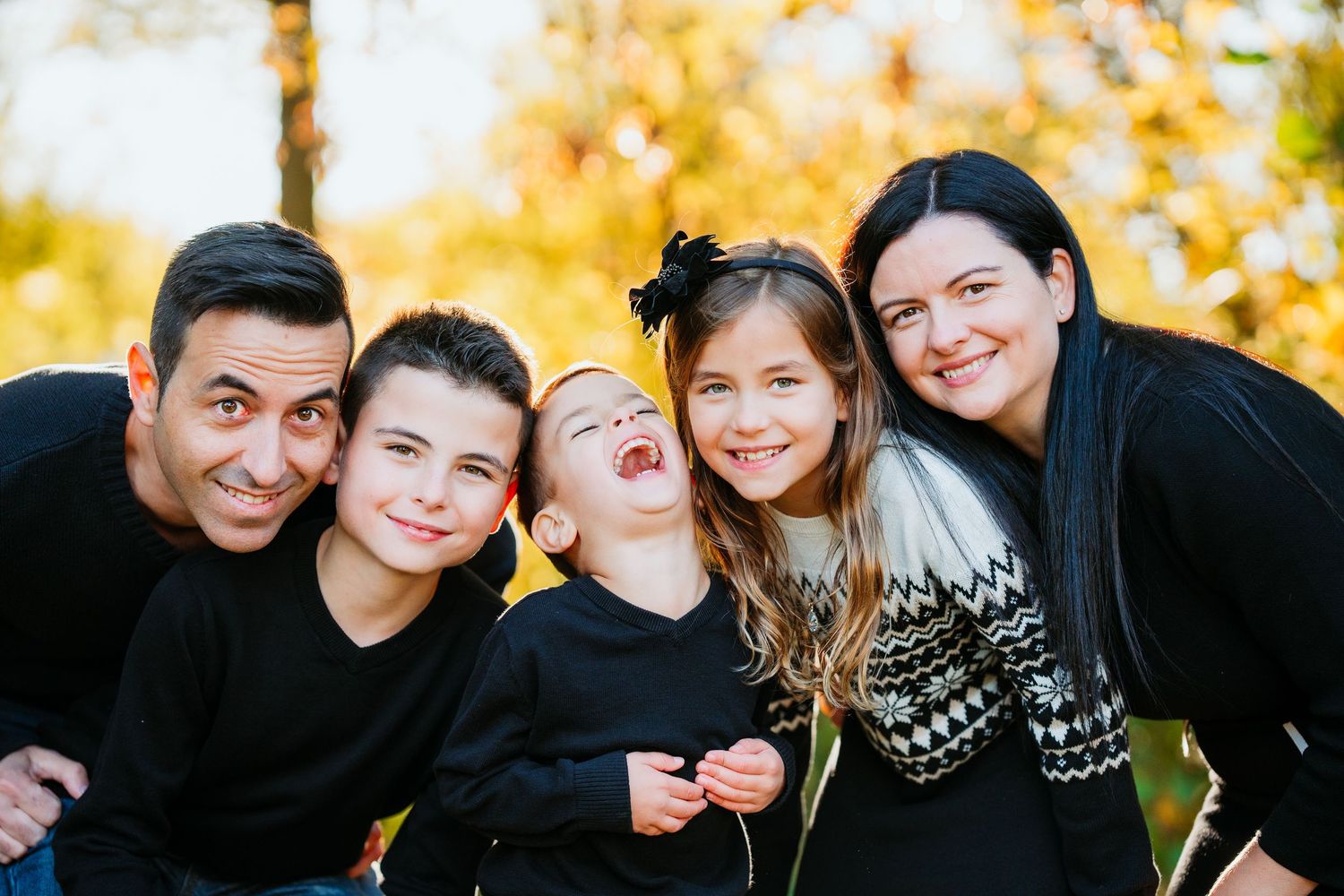 Family of five in matching black outfits laughing together during an outdoor fall family portrait session
