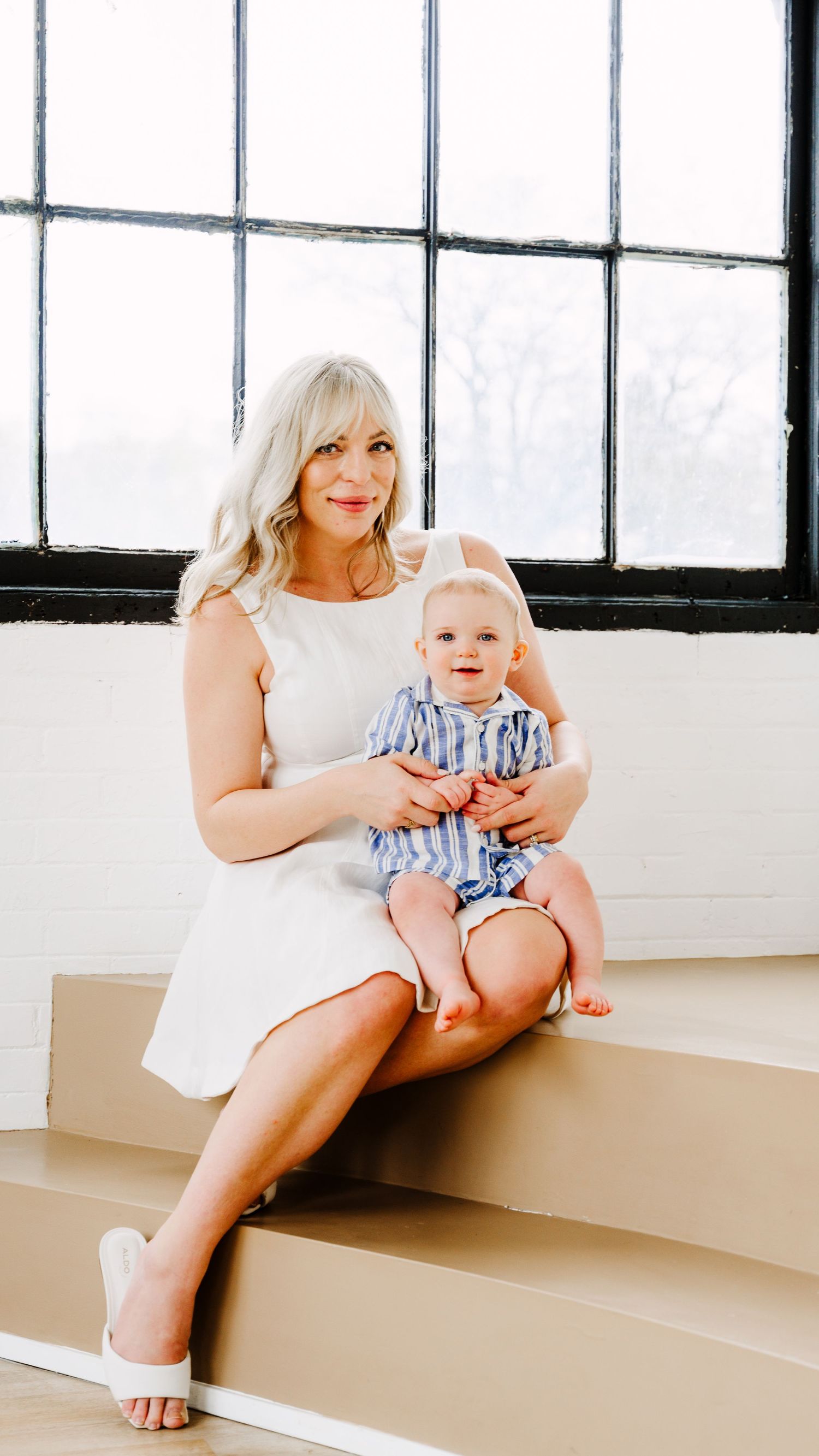 Mother sitting by a window holding a newborn baby in warm natural light