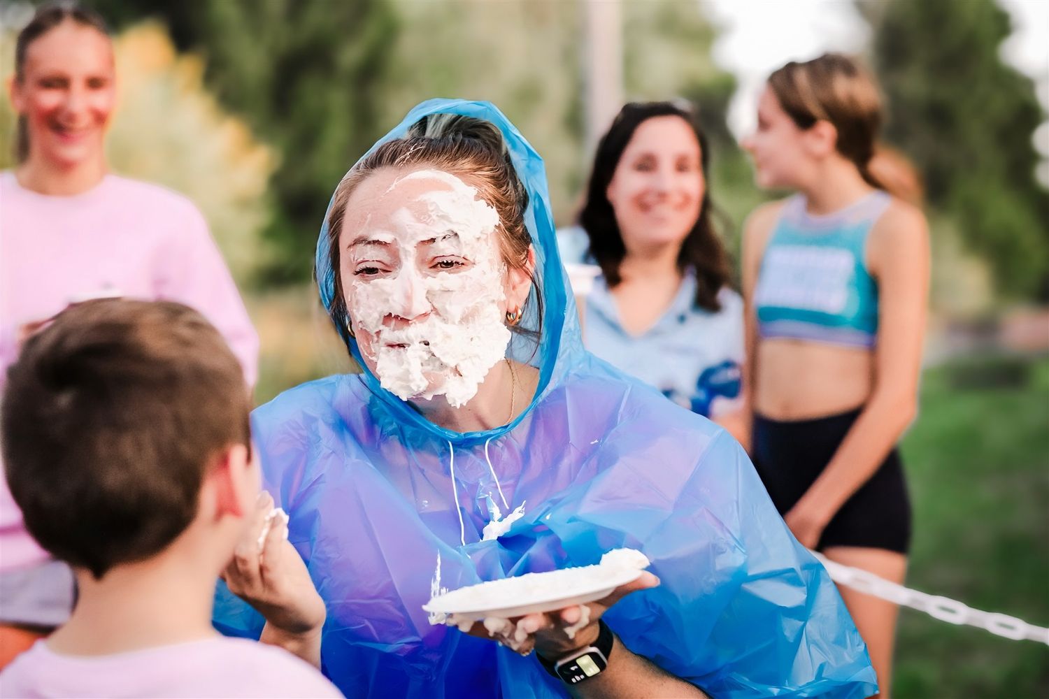 Coach playfully engaging with young cheerleaders, wearing a blue rain poncho during an outdoor event
