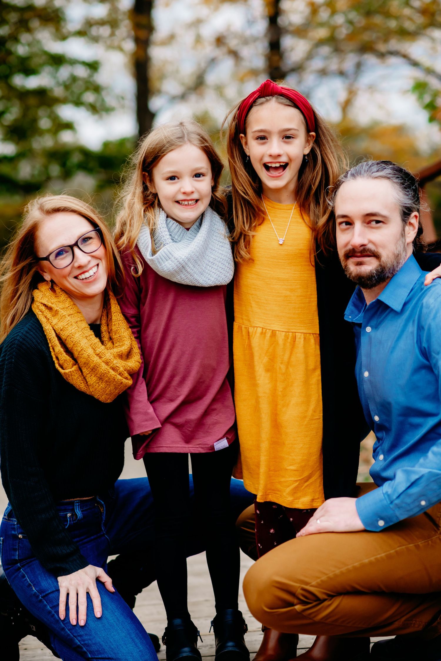 Family of five in coordinating warm-toned outfits smiling together during an outdoor fall portrait session