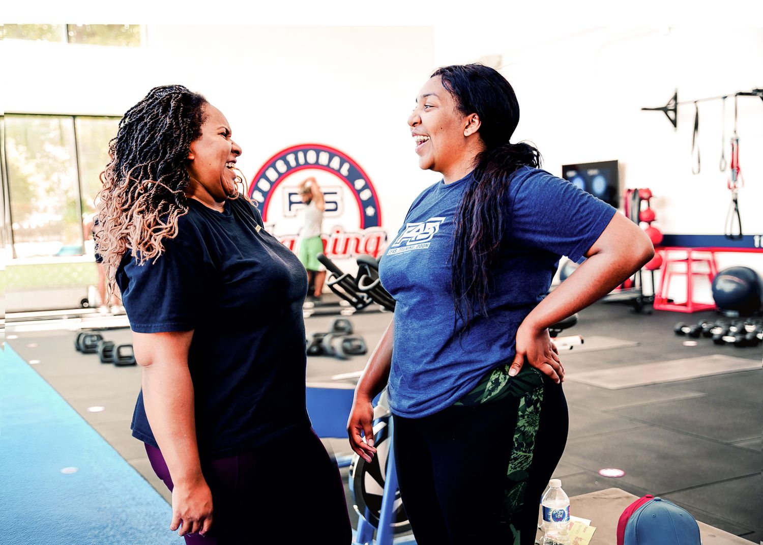 Two women smiling and interacting outdoors at a community or fitness event