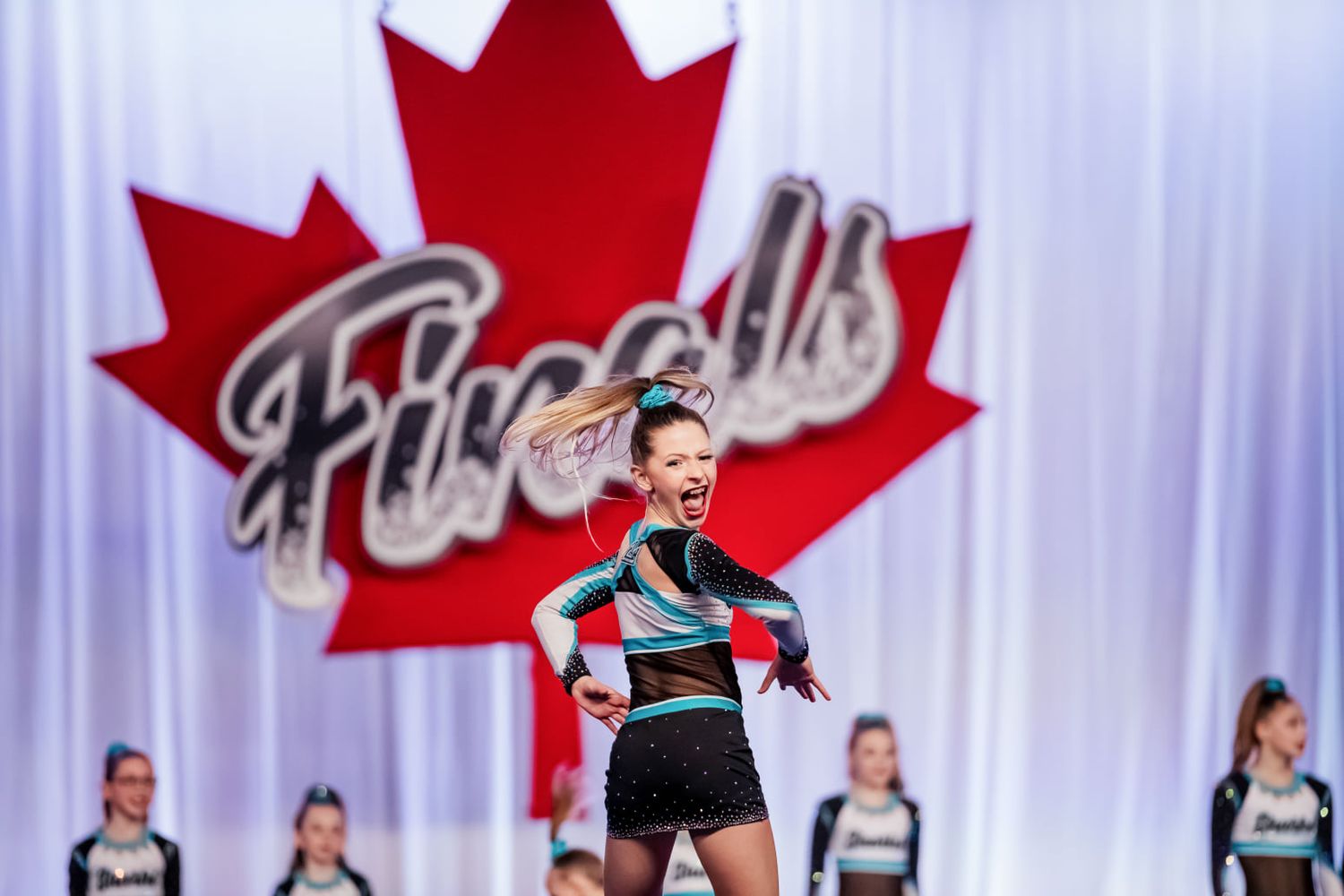 Cheerleading team posing in front of a large Canadian Maple Leaf Nationals Finals sign