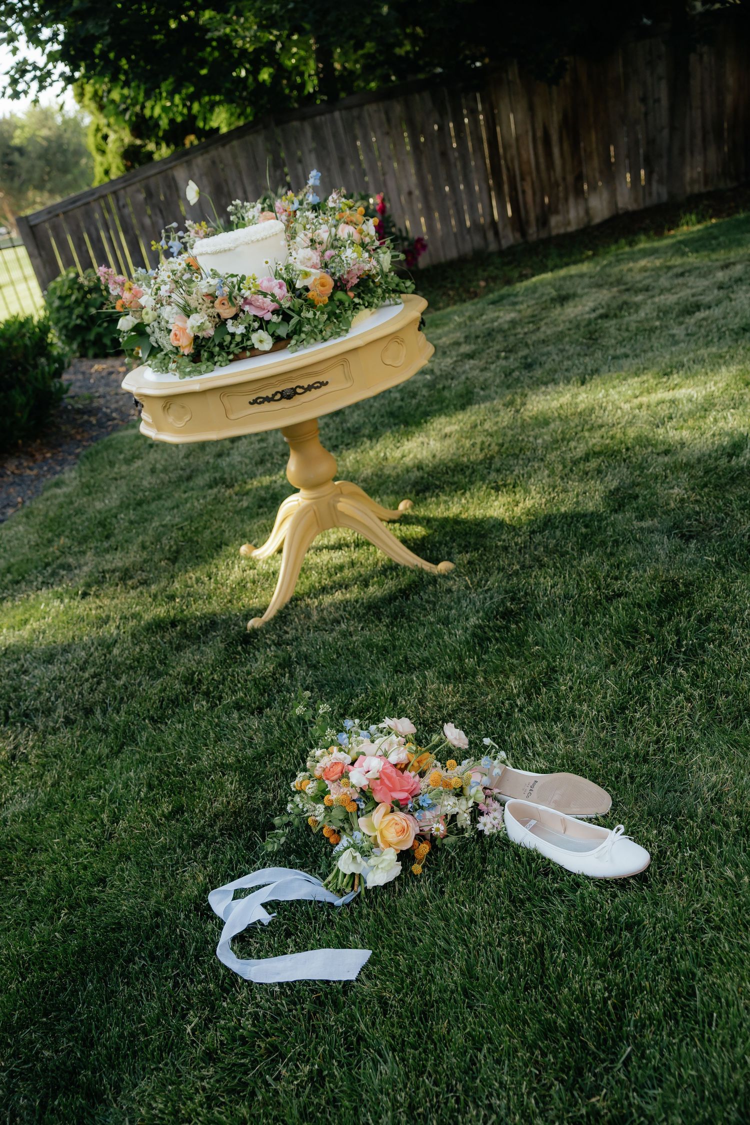 Wedding dessert table with floral arrangements displayed outdoors on grass with wedding bouquet and shoes. Outdoor summer, luxury wedding.