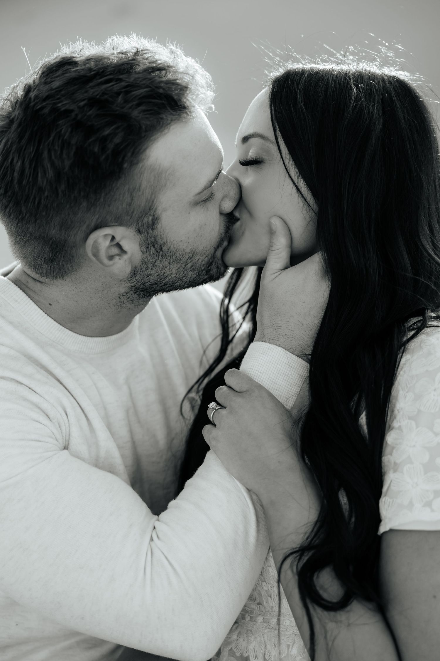 Black and white photo of couple kissing during golden hour sharing an intimate moment.