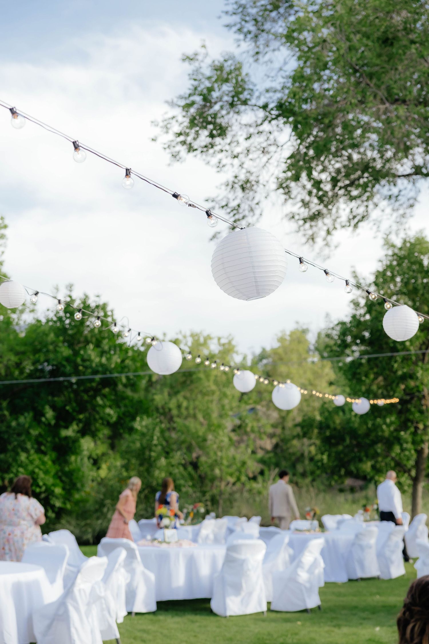 Outdoor wedding reception setup with string lights and white chairs