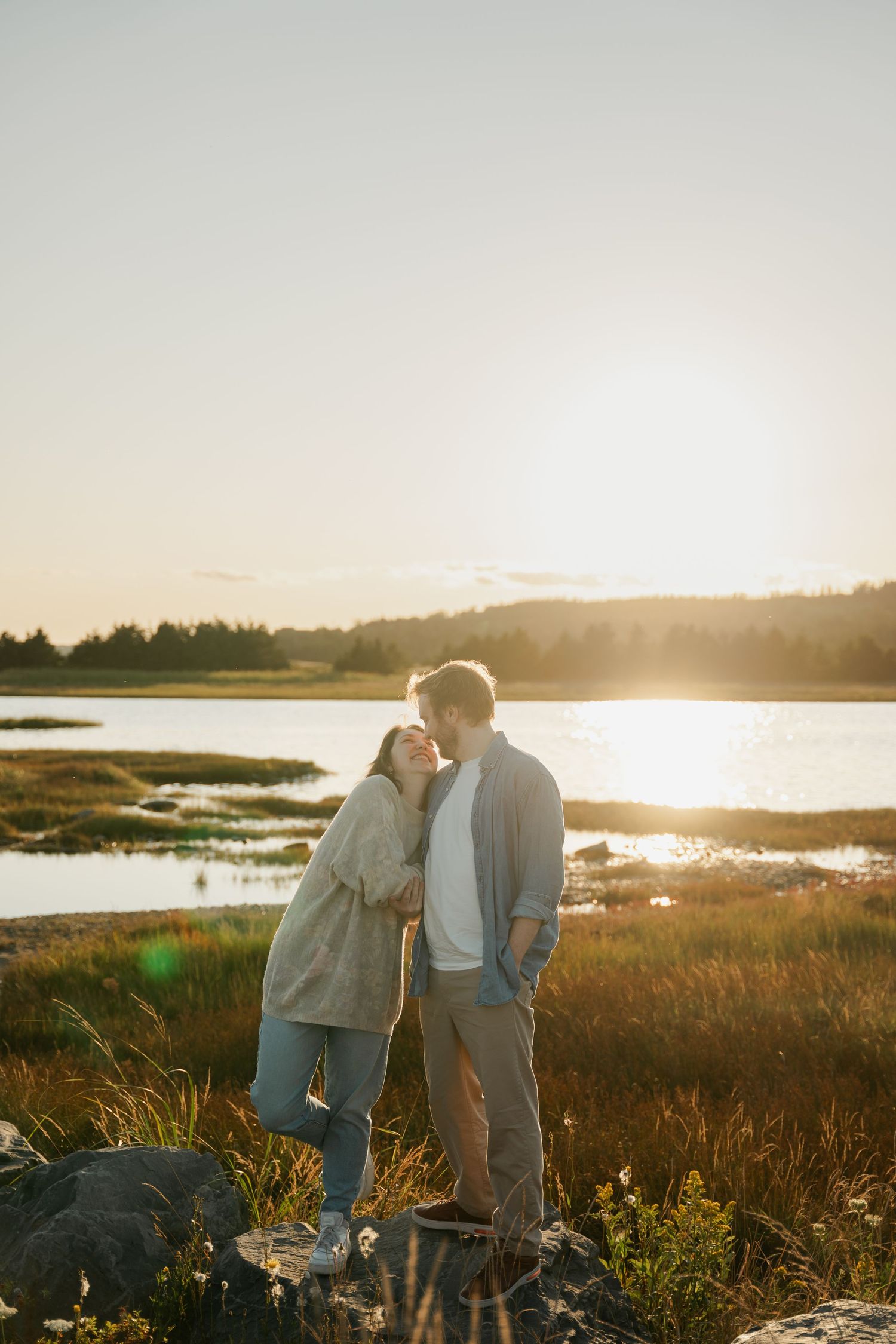Couple embraces while watching sunset over a serene marsh landscape in Halifax, Nova Scotia with golden light reflecting on the water.