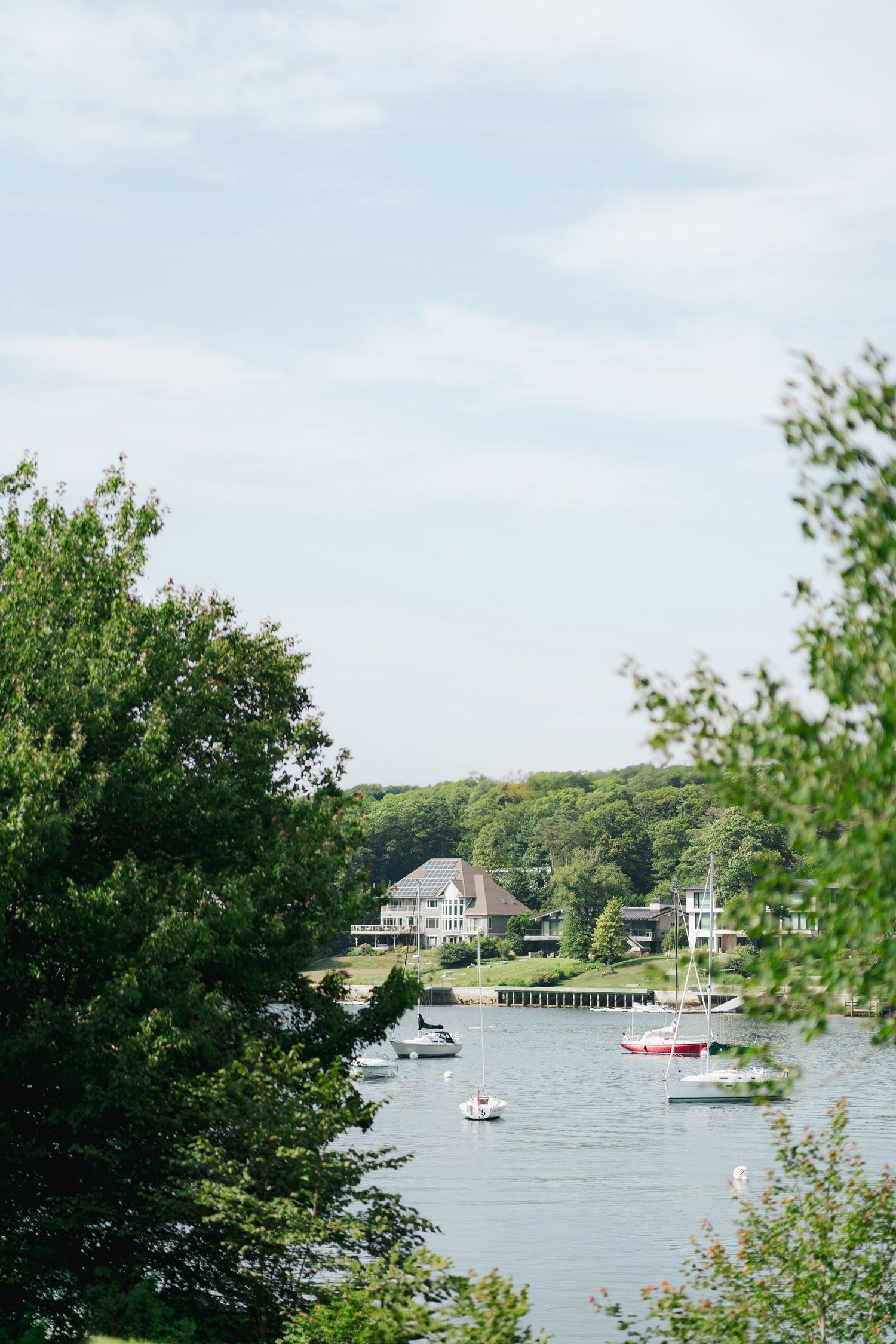 Scenic lakeside view with boats anchored in calm waters and houses nestled among trees on the distant shore in Halifax, Nova Scotia.