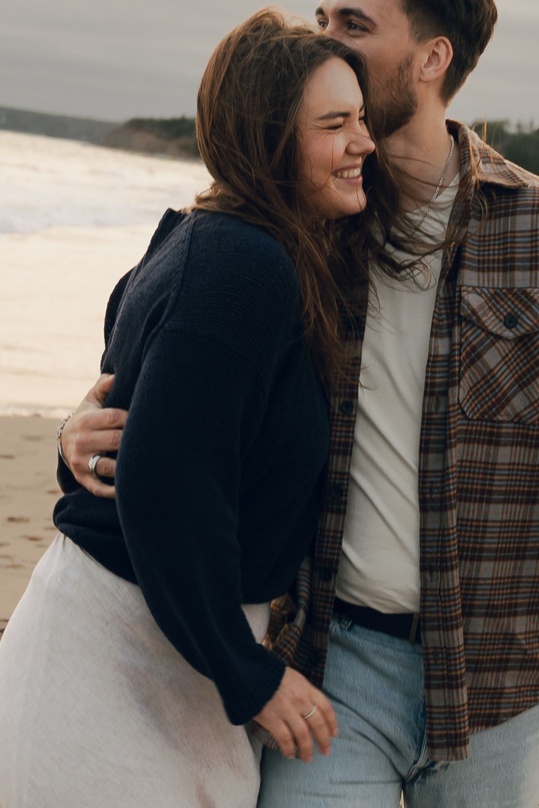 A couple shares intimate moments and laughter while embracing on a beach in Halifax, Nova Scotia during sunset.