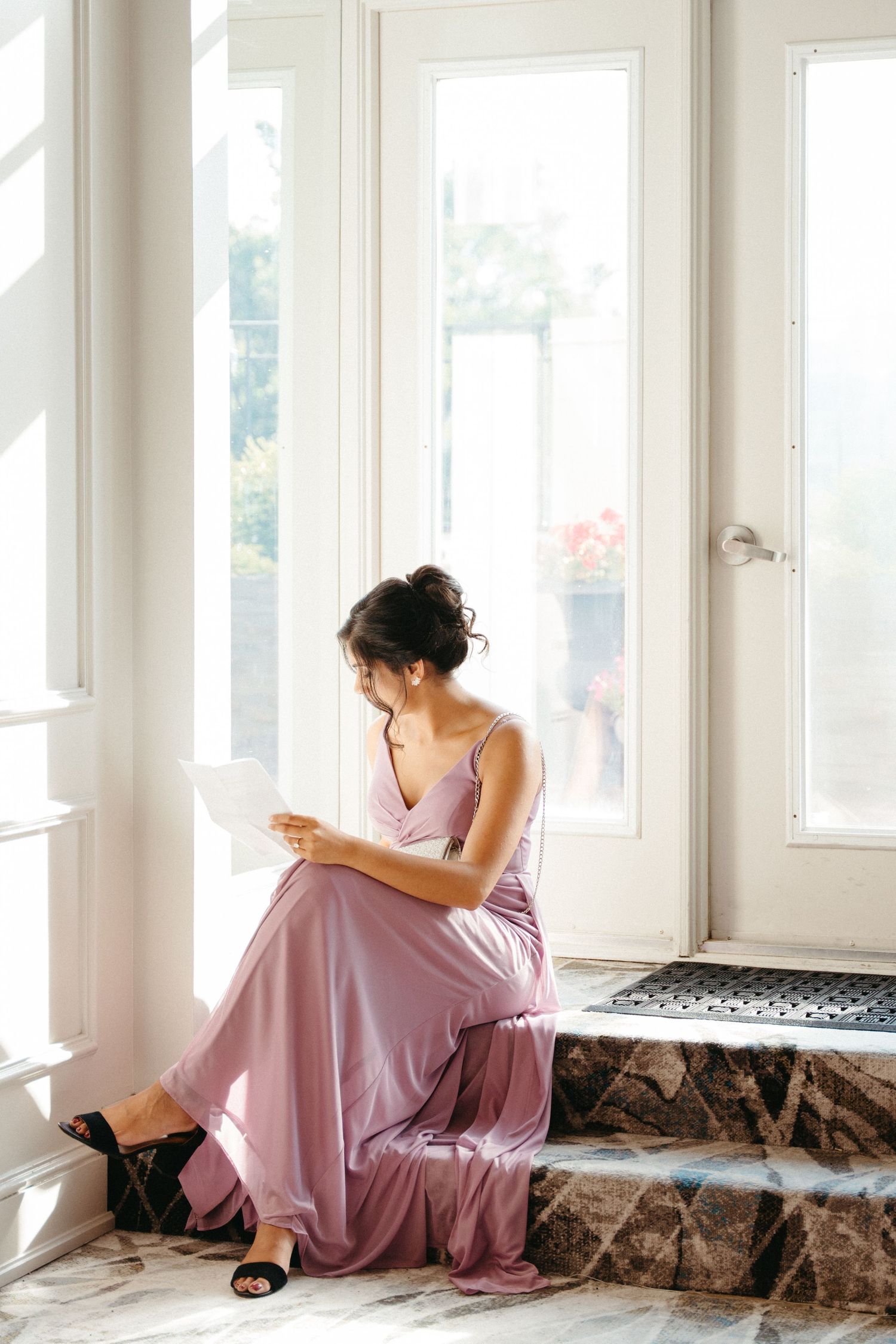 A person in a flowing pink dress sits contemplatively by a bright window with white frames in Halifax, Nova Scotia.